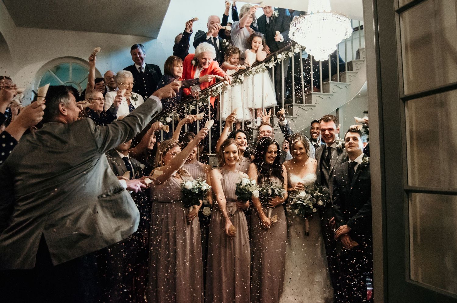 Large group celebration on staircase with confetti in the air.
