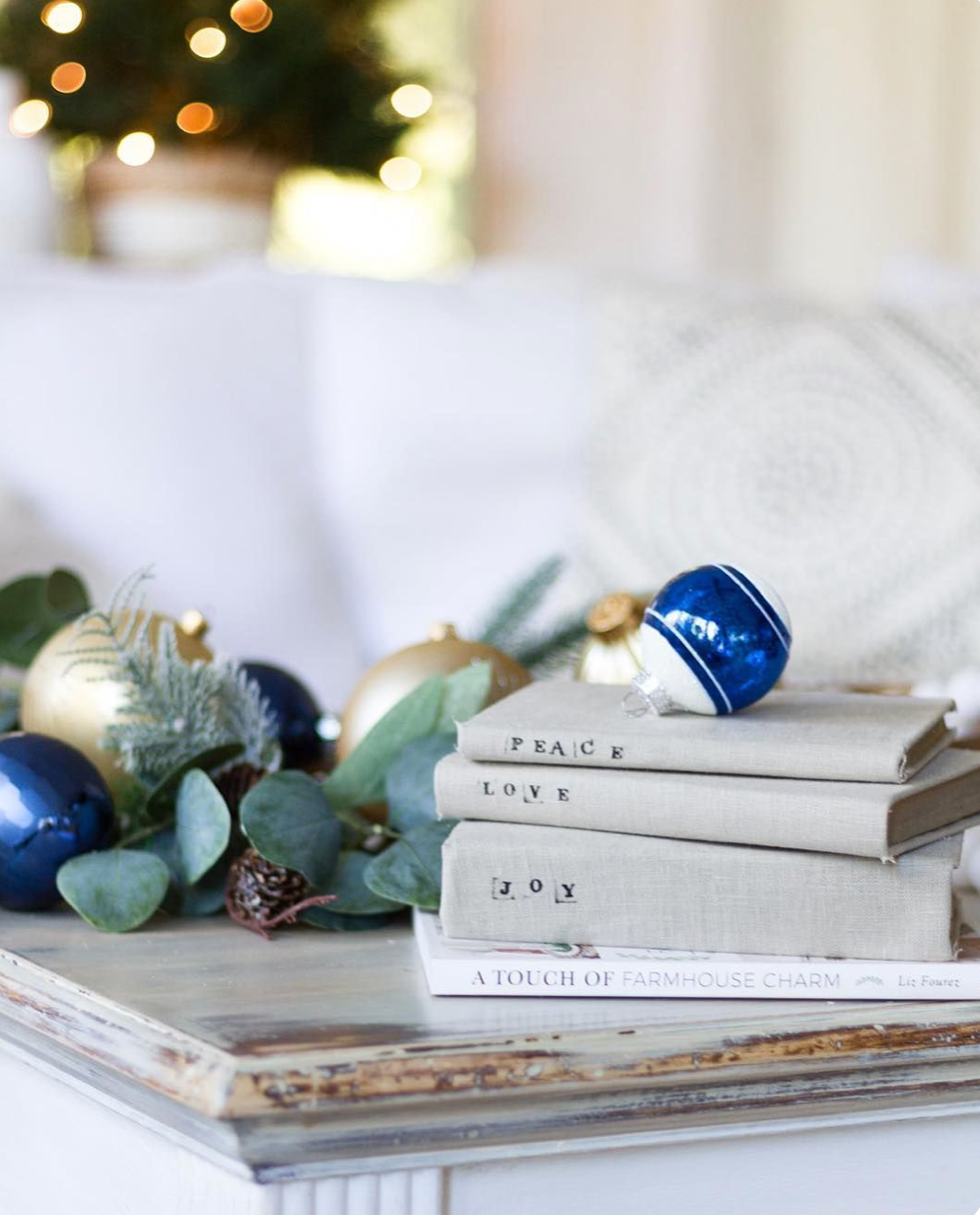 Stack of white books with blue and silver Christmas ornaments and eucalyptus branches against a soft blurred background.