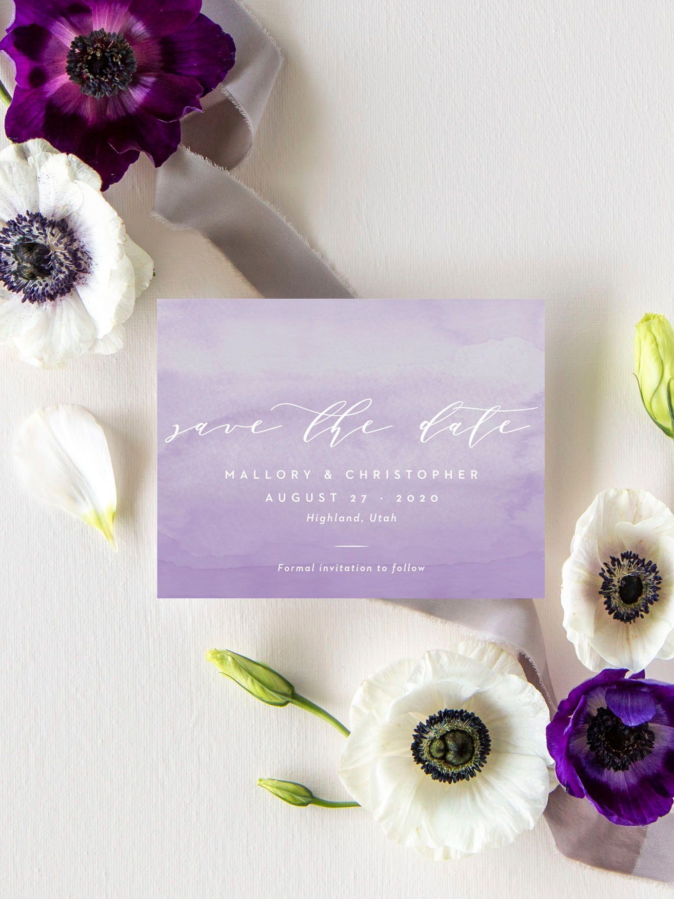 Purple and white anemone flowers surround a lavender watercolor save the date card on a white background.