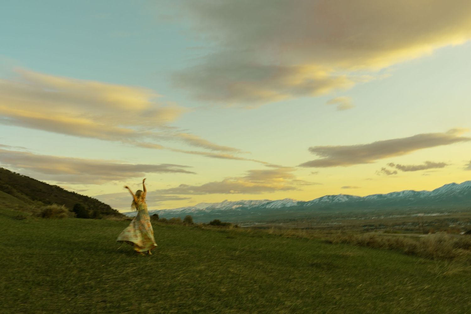 Senior pictures of a girl twirling around in a dress with colorful clouds at sunset