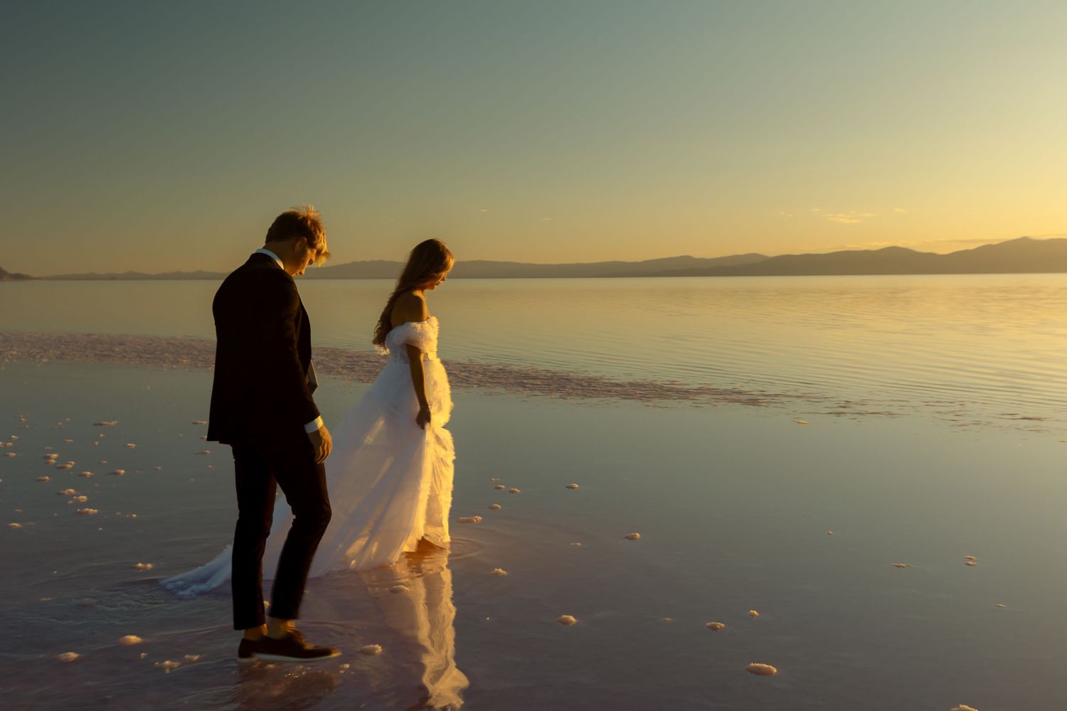 A bride and groom walking at a Pink Lake in a wedding dress