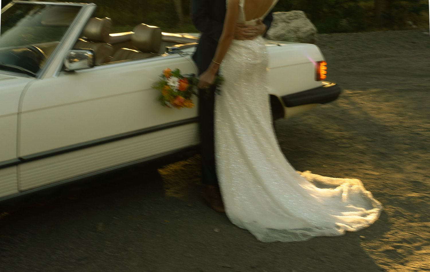 a bride and groom with a vintage car on their wedding day with wedding dress and bouquet
