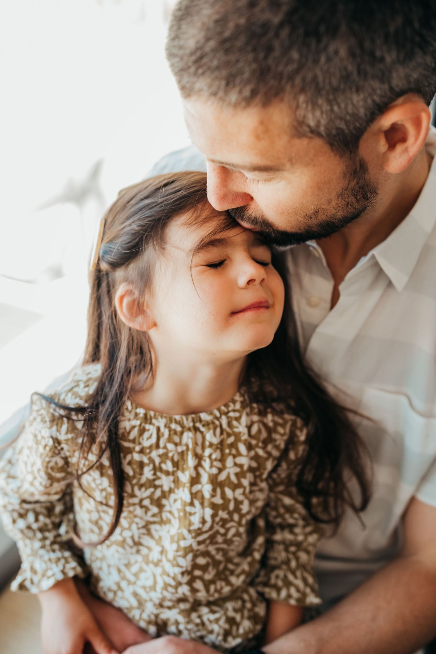 A father kisses his daughter's forehead as she embraces his love.