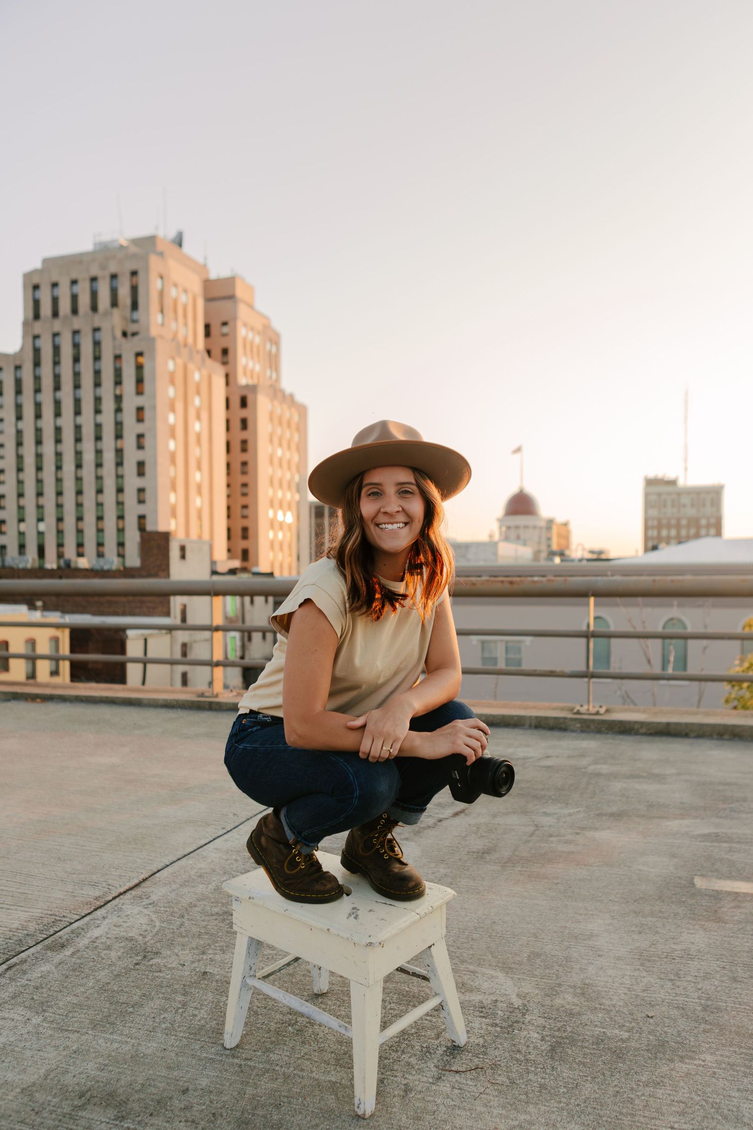 A casual portrait session on an urban rooftop with a person posing on a white wooden stool at sunset.