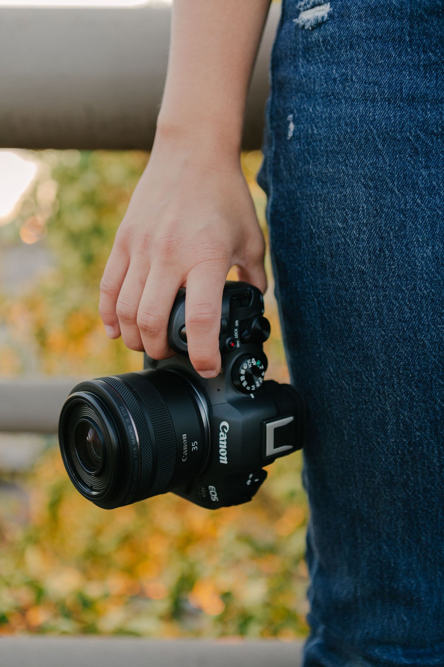 Close-up shot of hands holding a Canon camera against blue denim jeans.