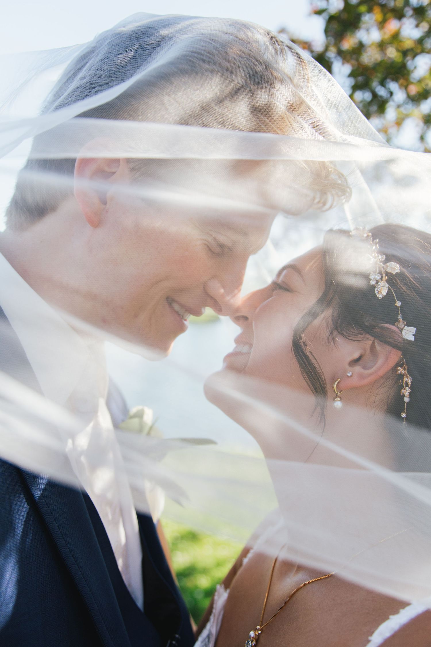 Romantic wedding couple sharing an intimate moment under a flowing veil with sunlight streaming through.