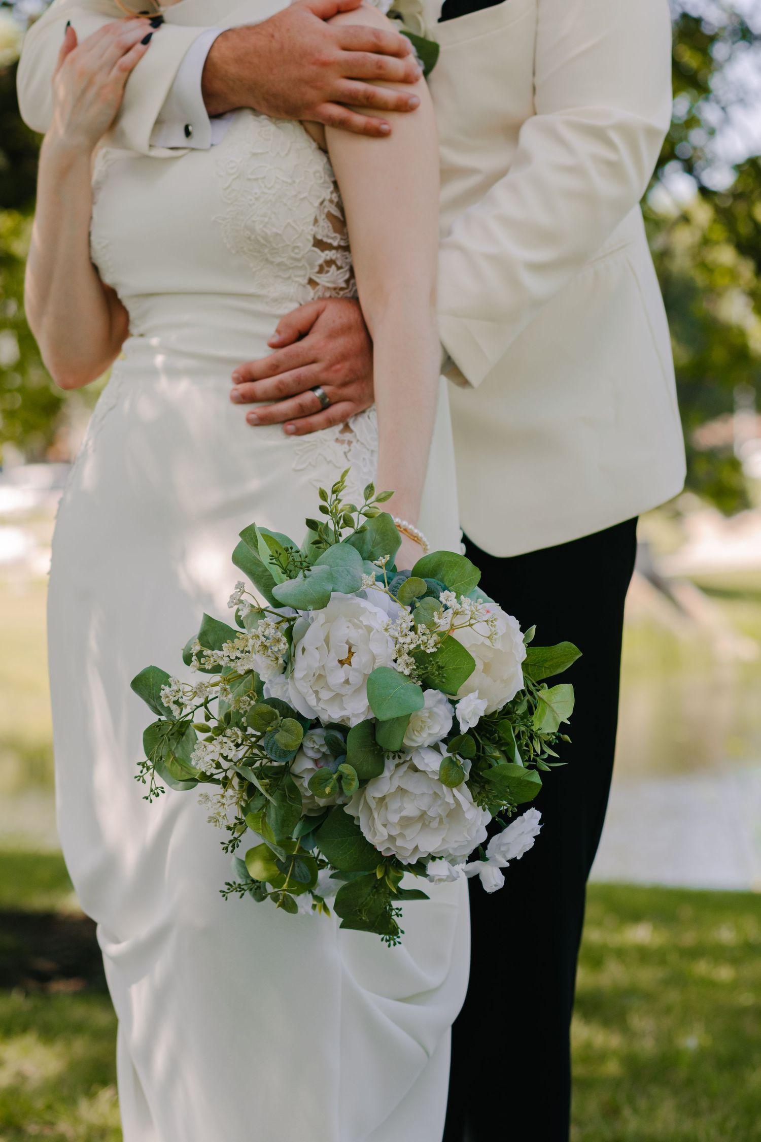 Wedding couple embracing outdoors with white floral bouquet and formal attire.