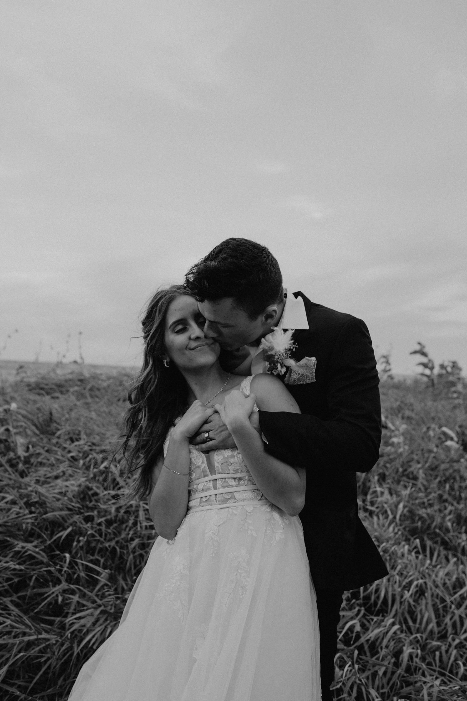A tender moment between newlyweds captured in black and white photography outdoors.