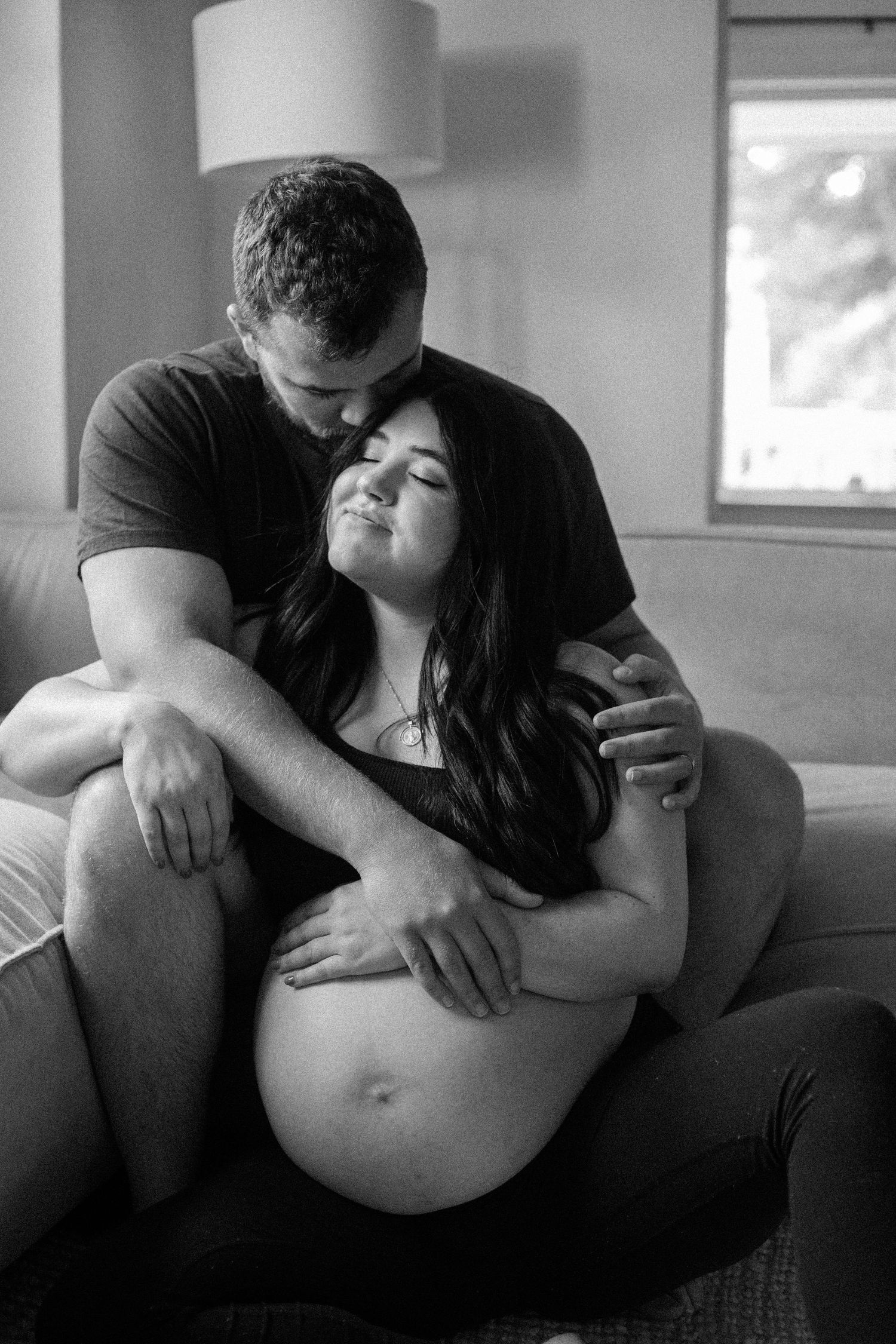 Intimate black and white maternity photos showing couple embracing on couch.