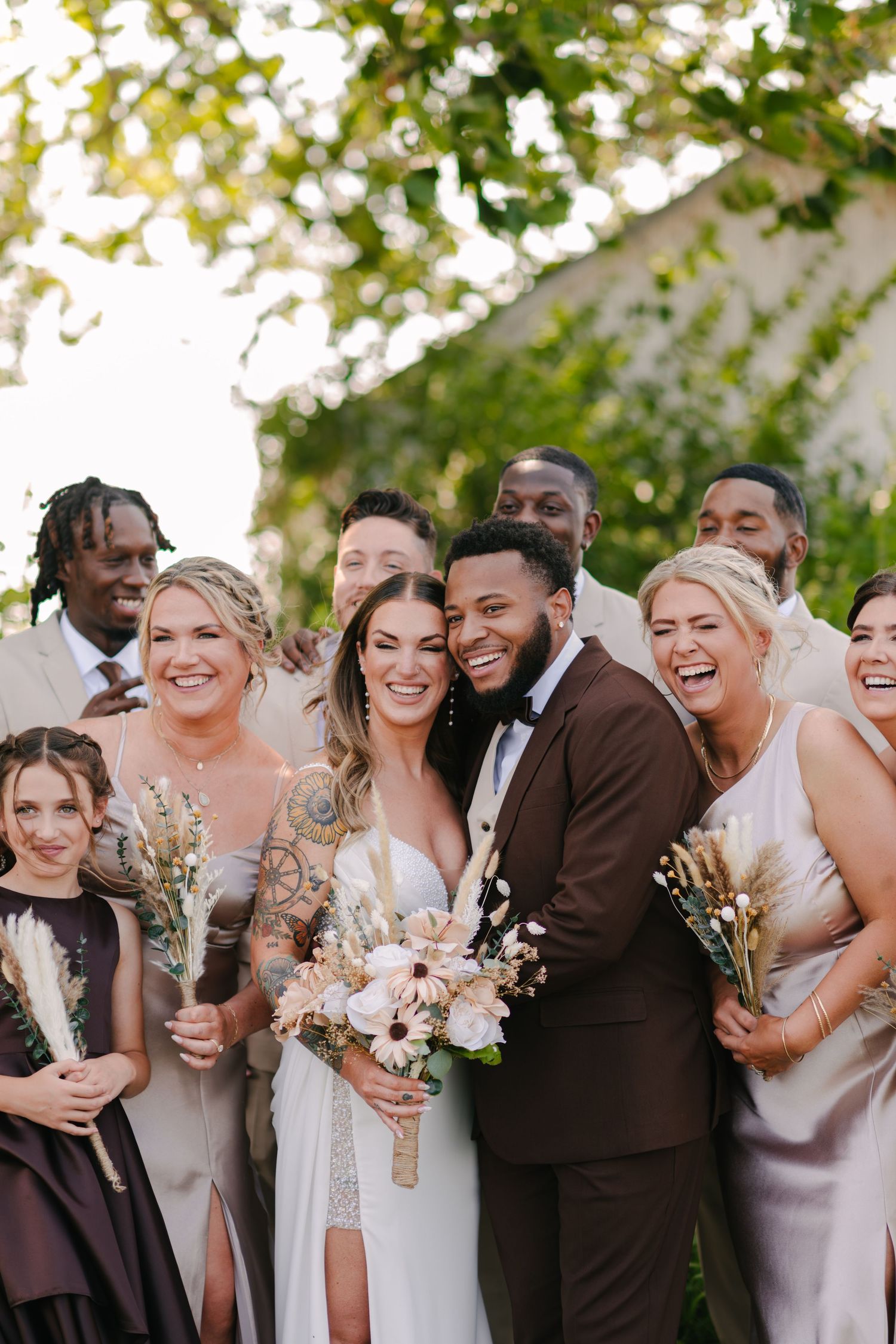 Wedding party in brown and blush colors posing together with bouquets outdoors.