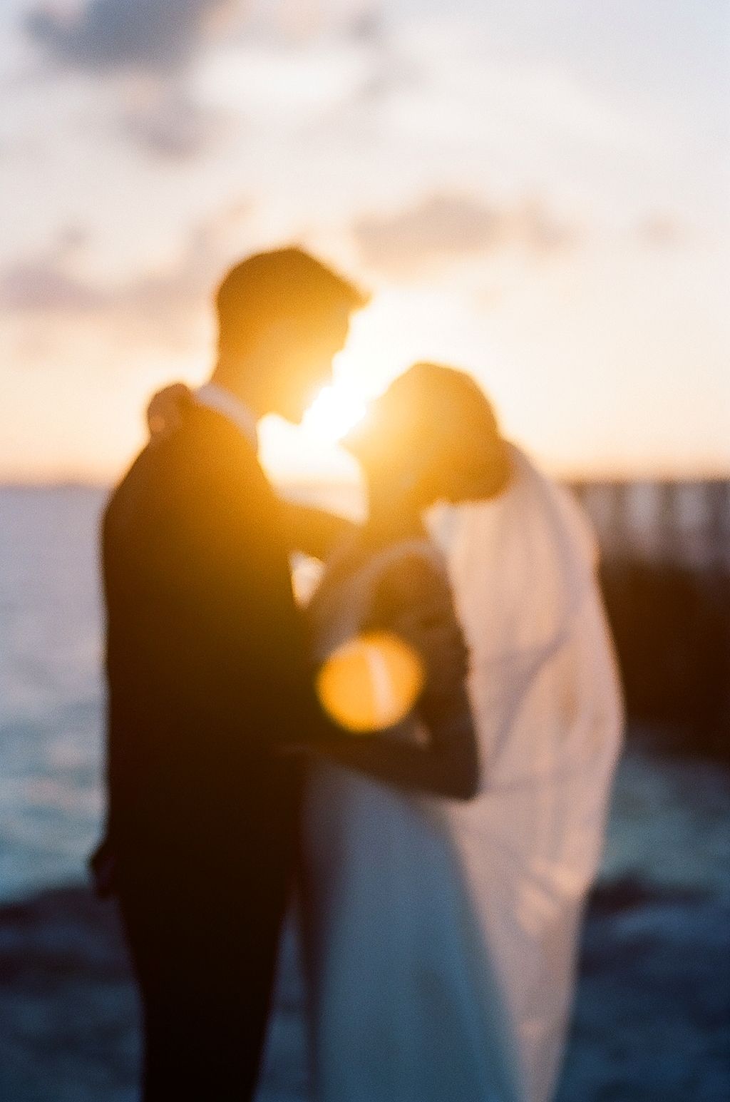 A silhouetted couple embraces against a golden sunset over the water.