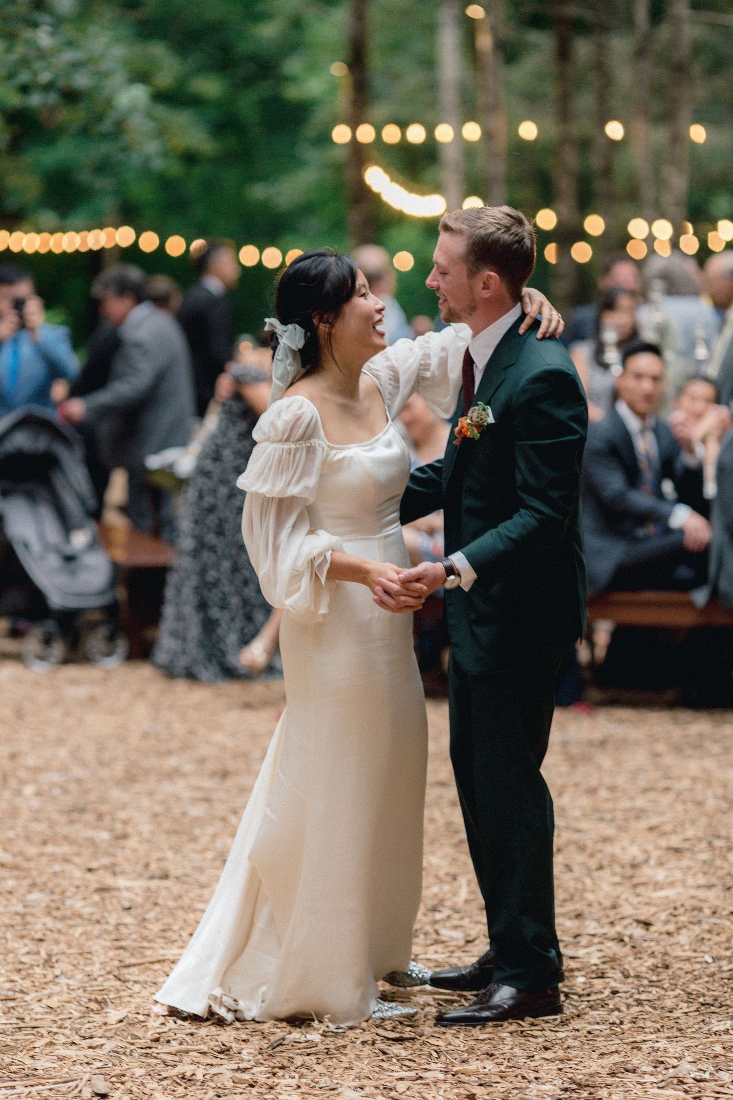 A couple dances under string lights at an outdoor wedding reception.