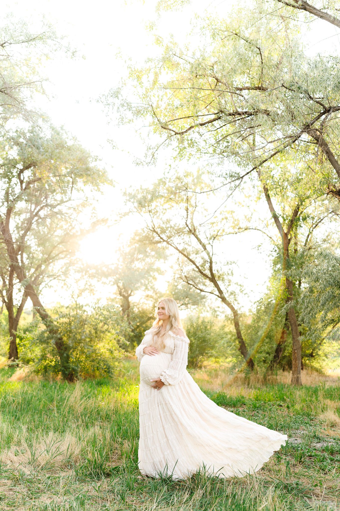 White dress flowing in a dreamy outdoor setting with golden sunlight filtering through trees.