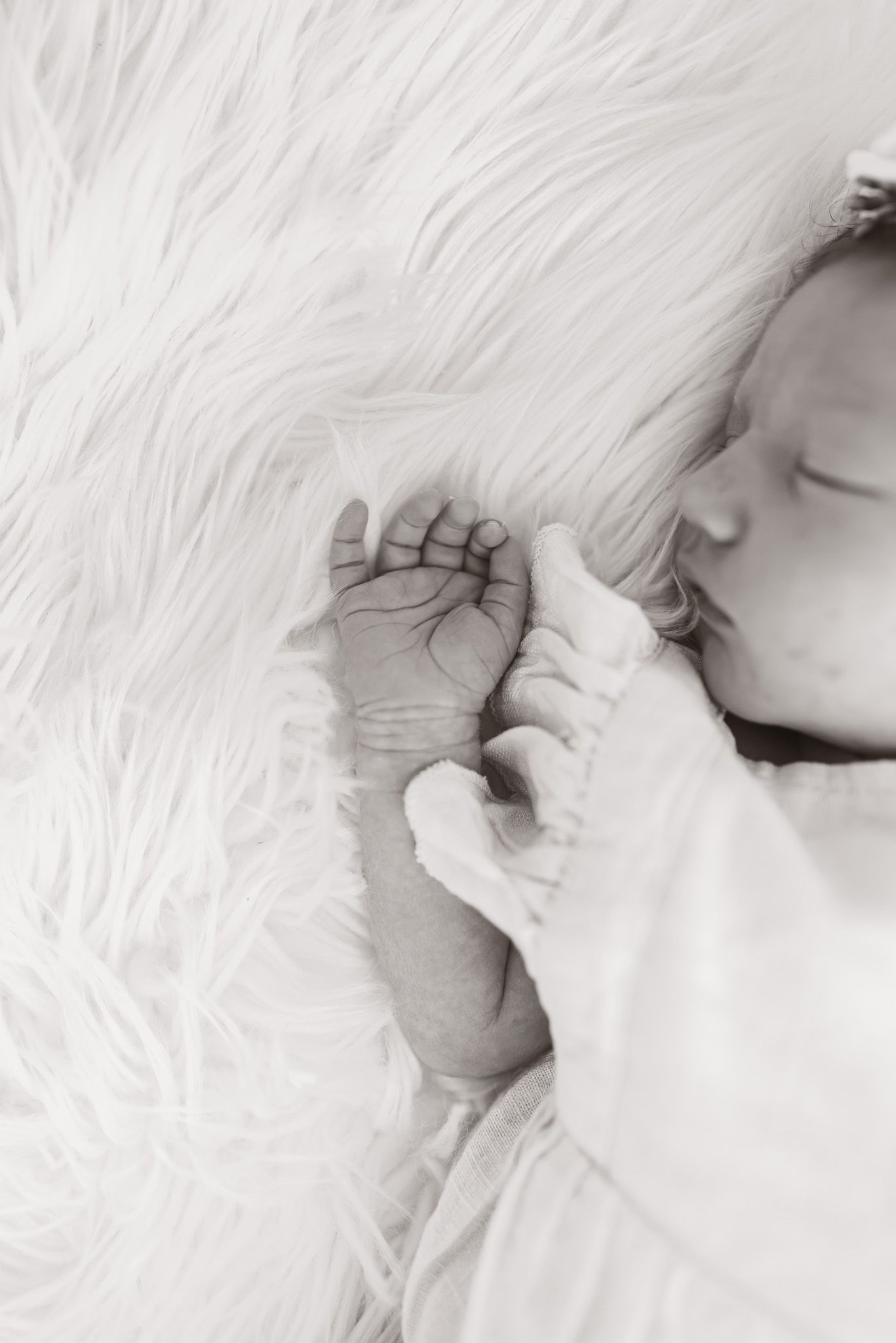 Black and white close-up of tiny baby feet against soft white fur background.