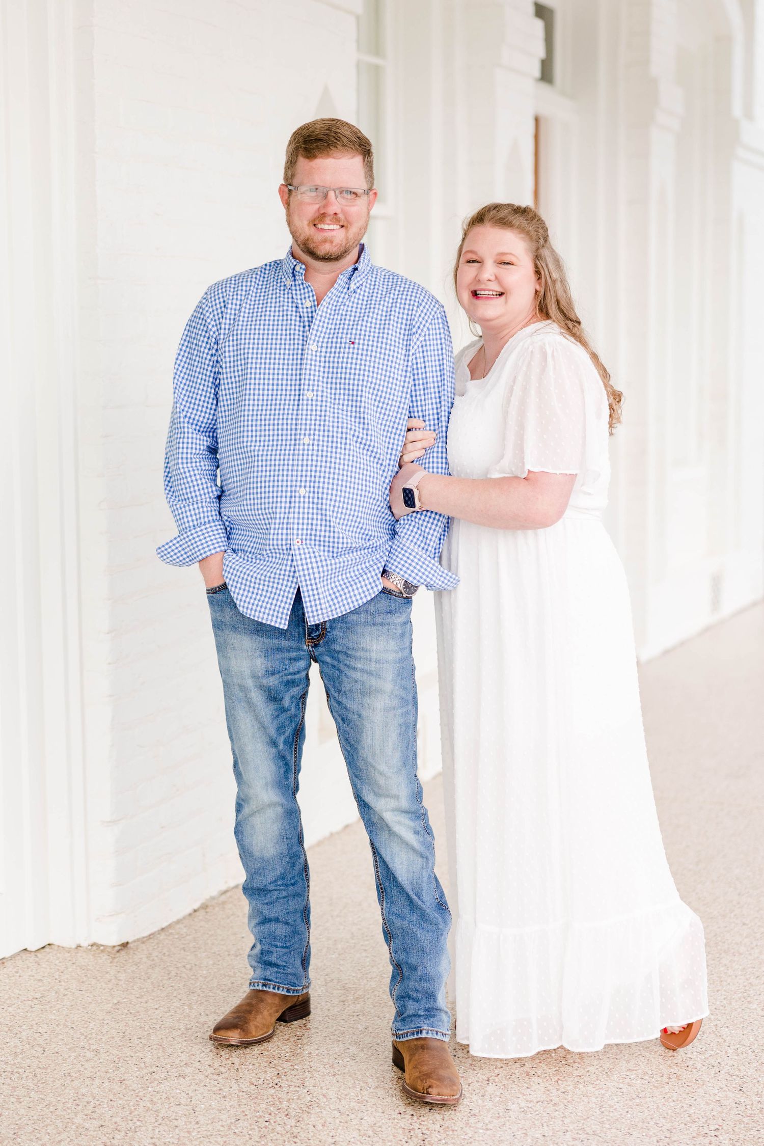 A couple poses together in a bright white hallway wearing coordinated blue and white outfits.