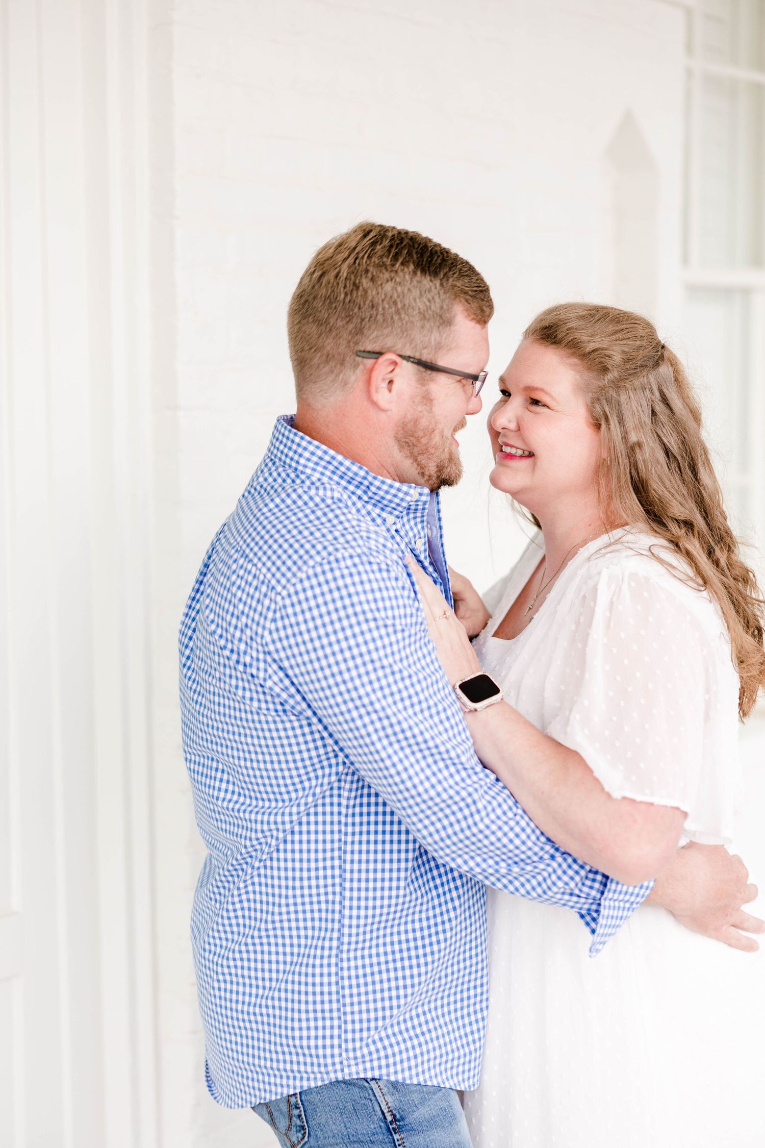 A couple laughs together during an intimate photoshoot in a bright white hallway.