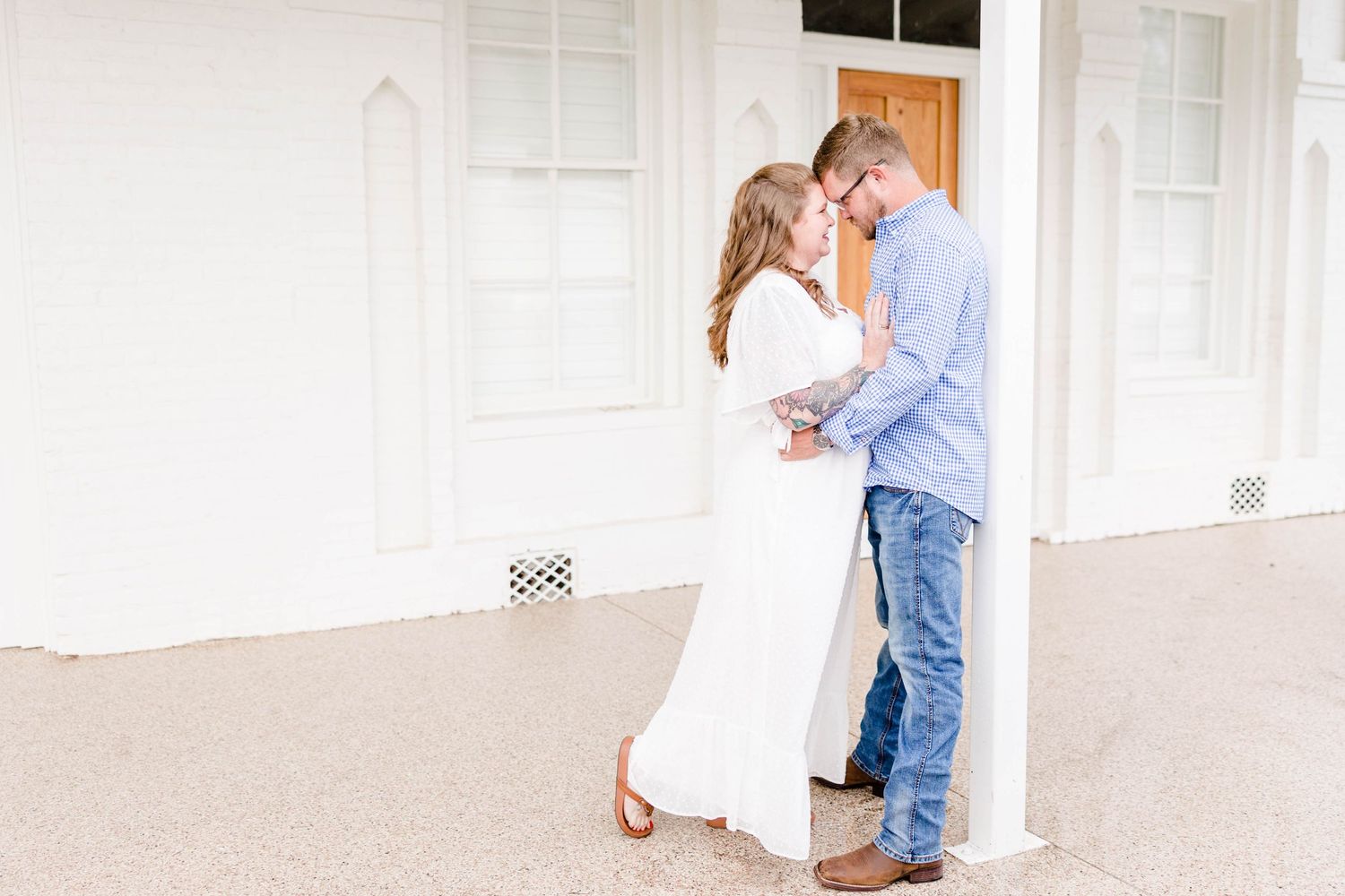 A couple poses together in a bright white hallway during an engagement session.