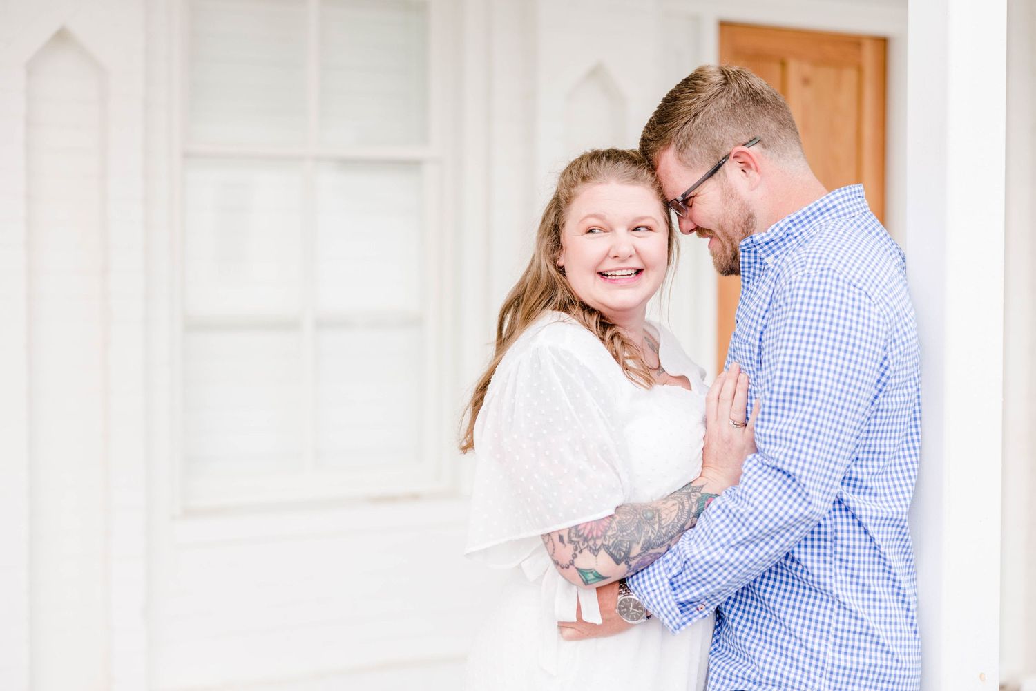 A couple embraces tenderly in a bright white hallway with wooden door accents.