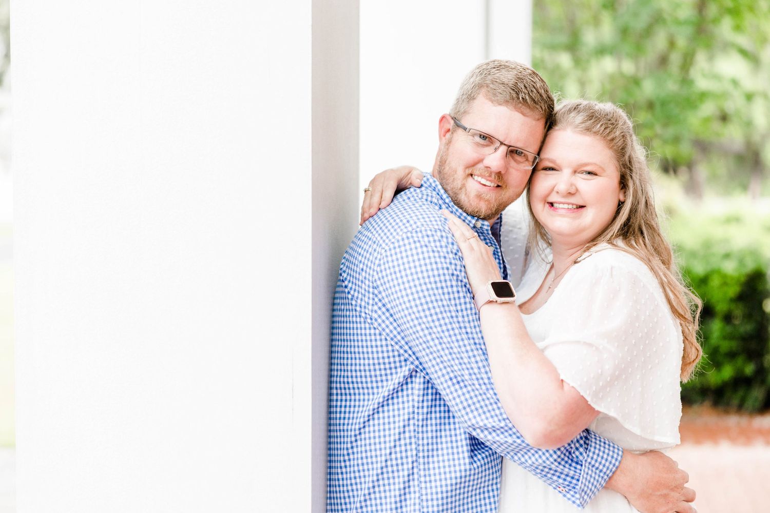 A happy couple shares a tender moment while posing against a white pillar.