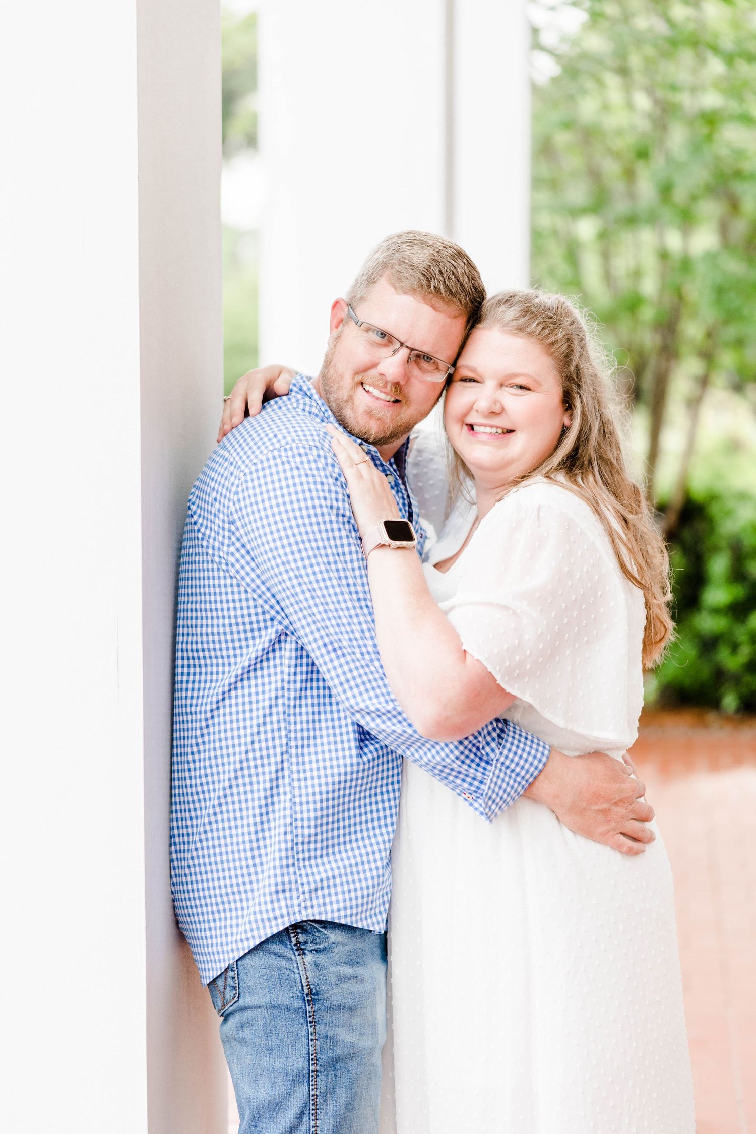 A loving couple shares an embrace while standing against a white column.