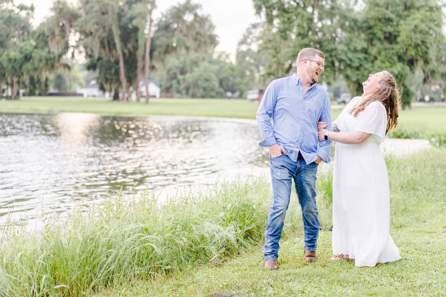 A couple shares a joyful moment beside a tranquil lake surrounded by Spanish moss trees.