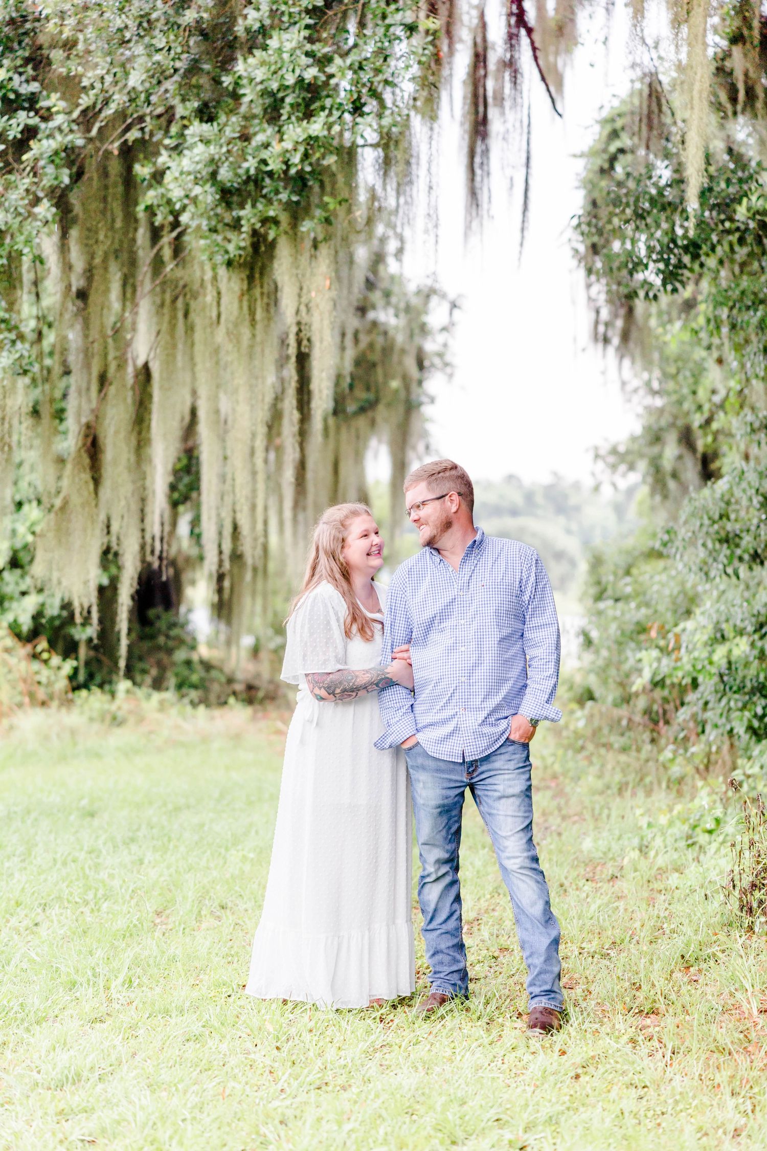 A couple stands beneath dramatic Spanish moss in a romantic Southern setting.