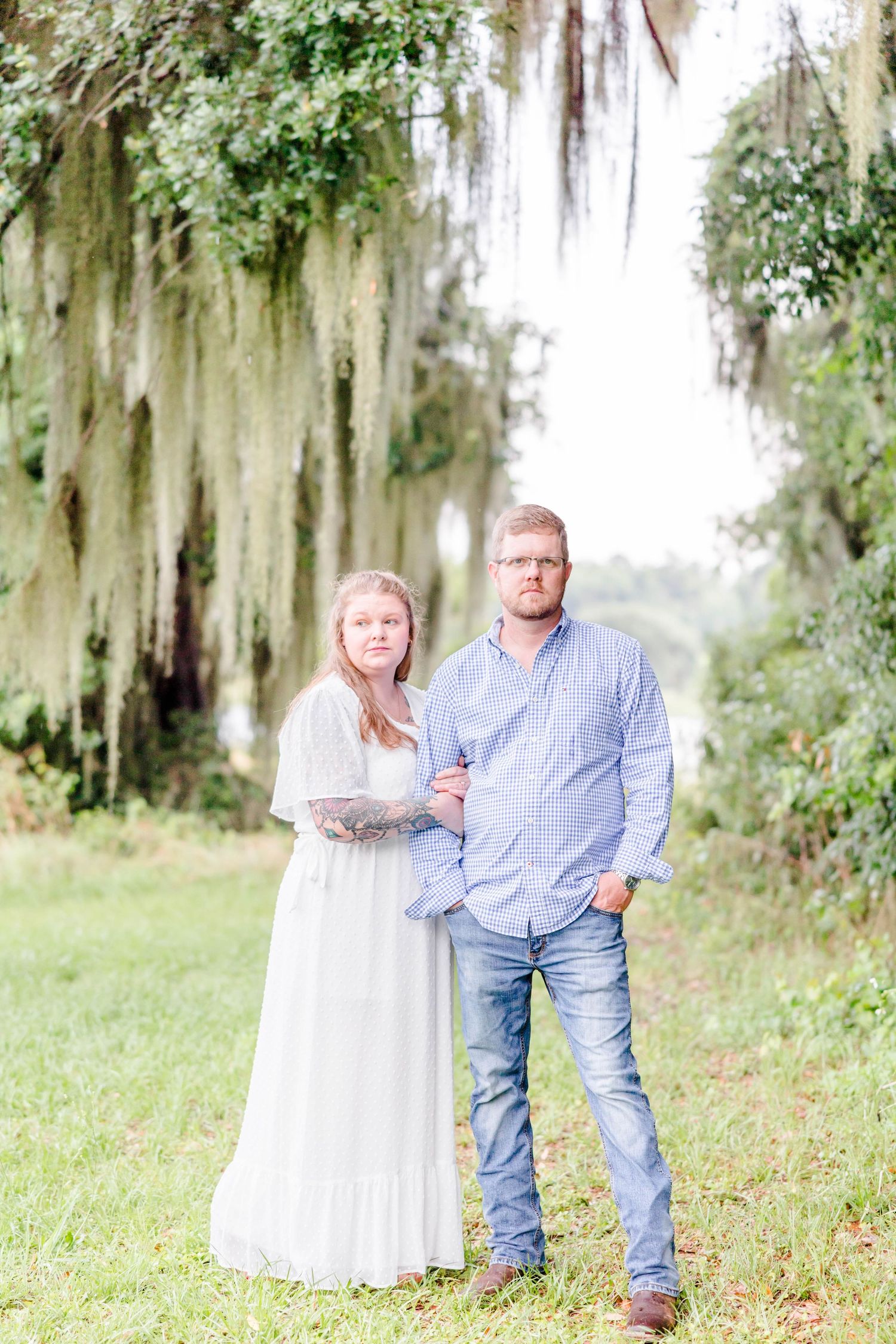 A couple poses together under hanging moss in a dreamy outdoor setting.