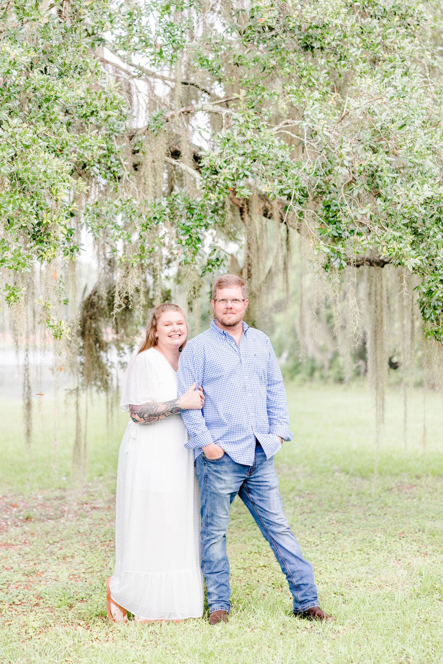 A couple poses beneath Spanish moss in a serene outdoor setting.