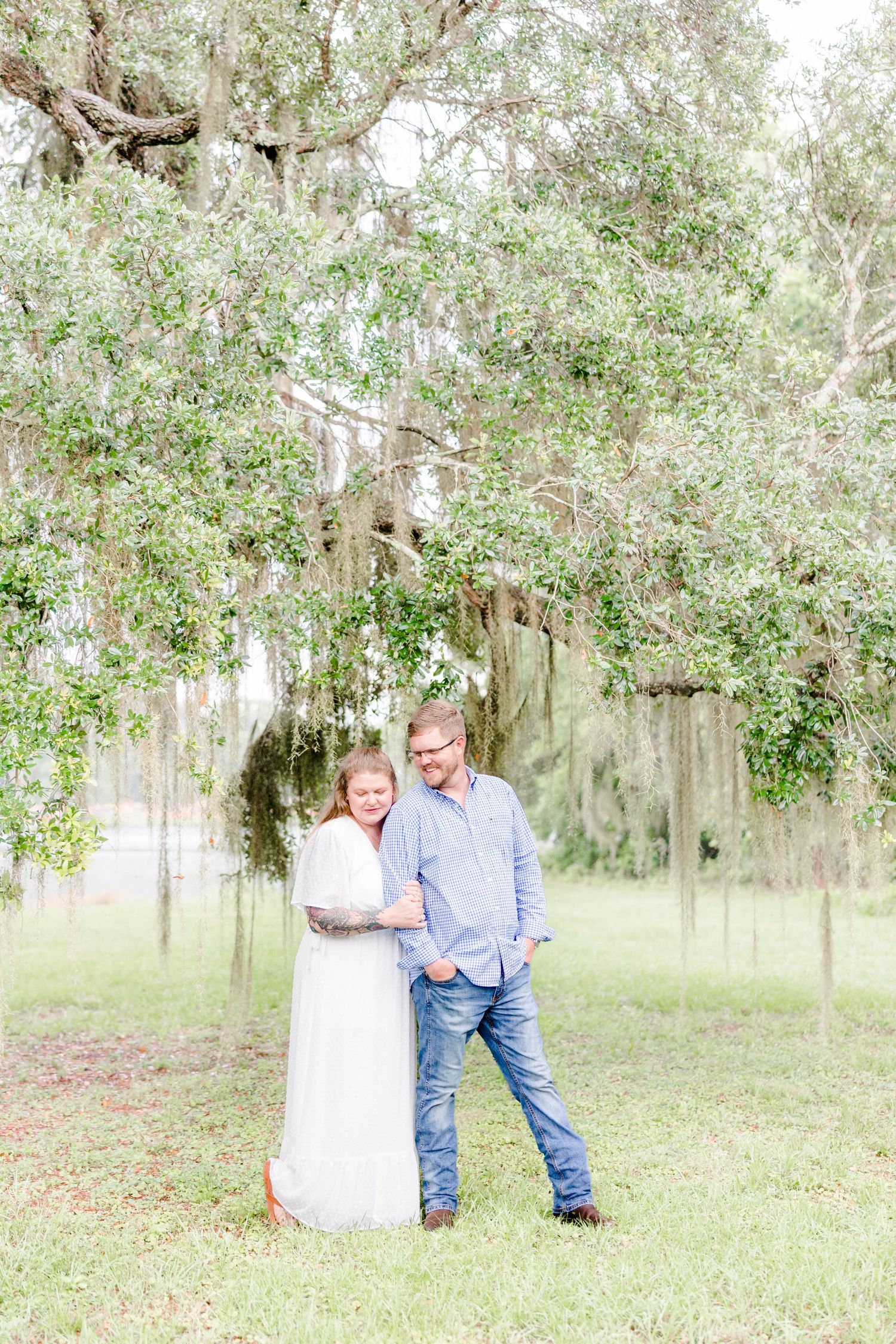 A couple shares a moment under Spanish moss hanging from oak trees.