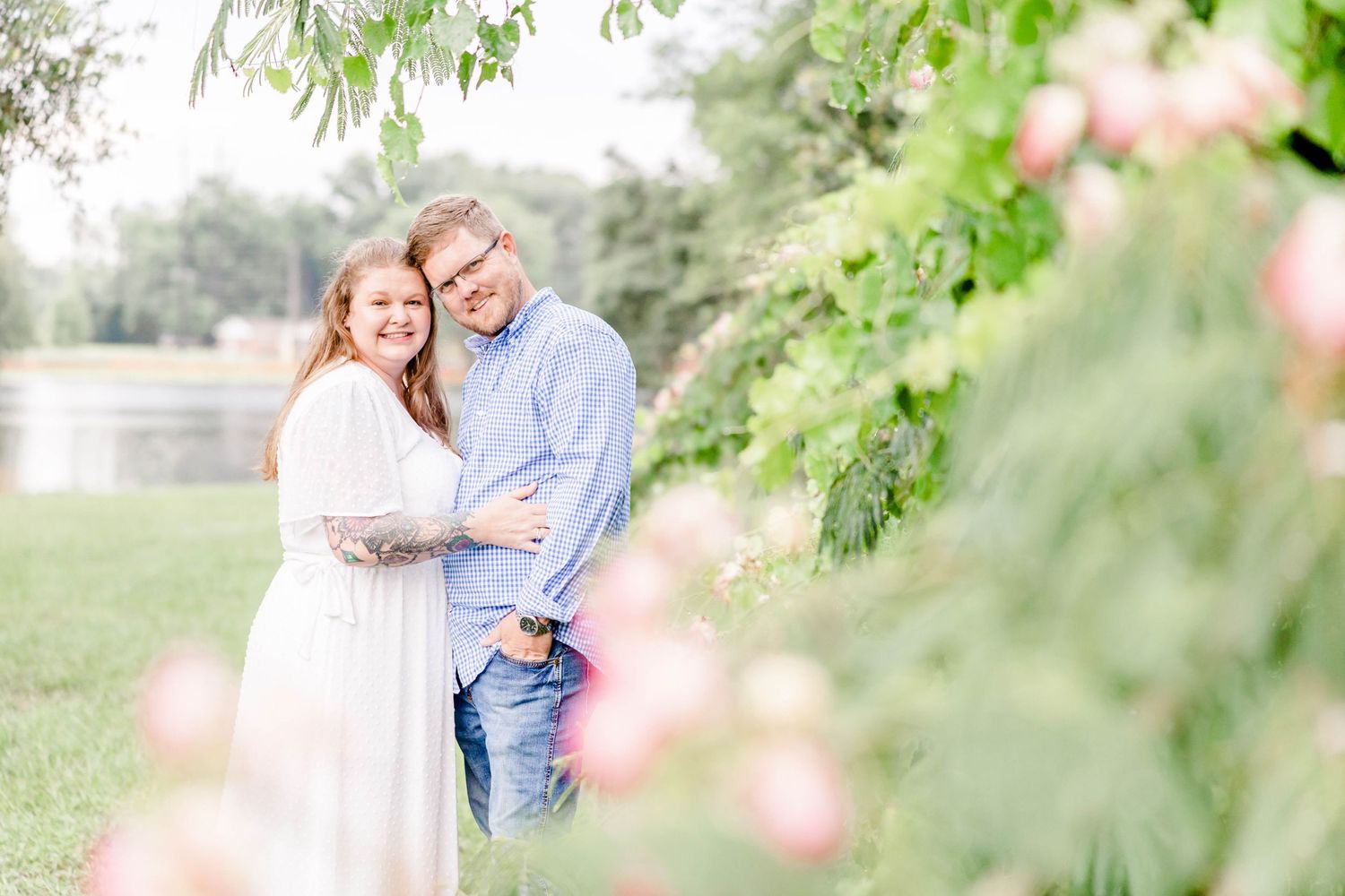 A romantic engagement photo of a couple embracing in a dreamy garden setting with soft natural lighting.