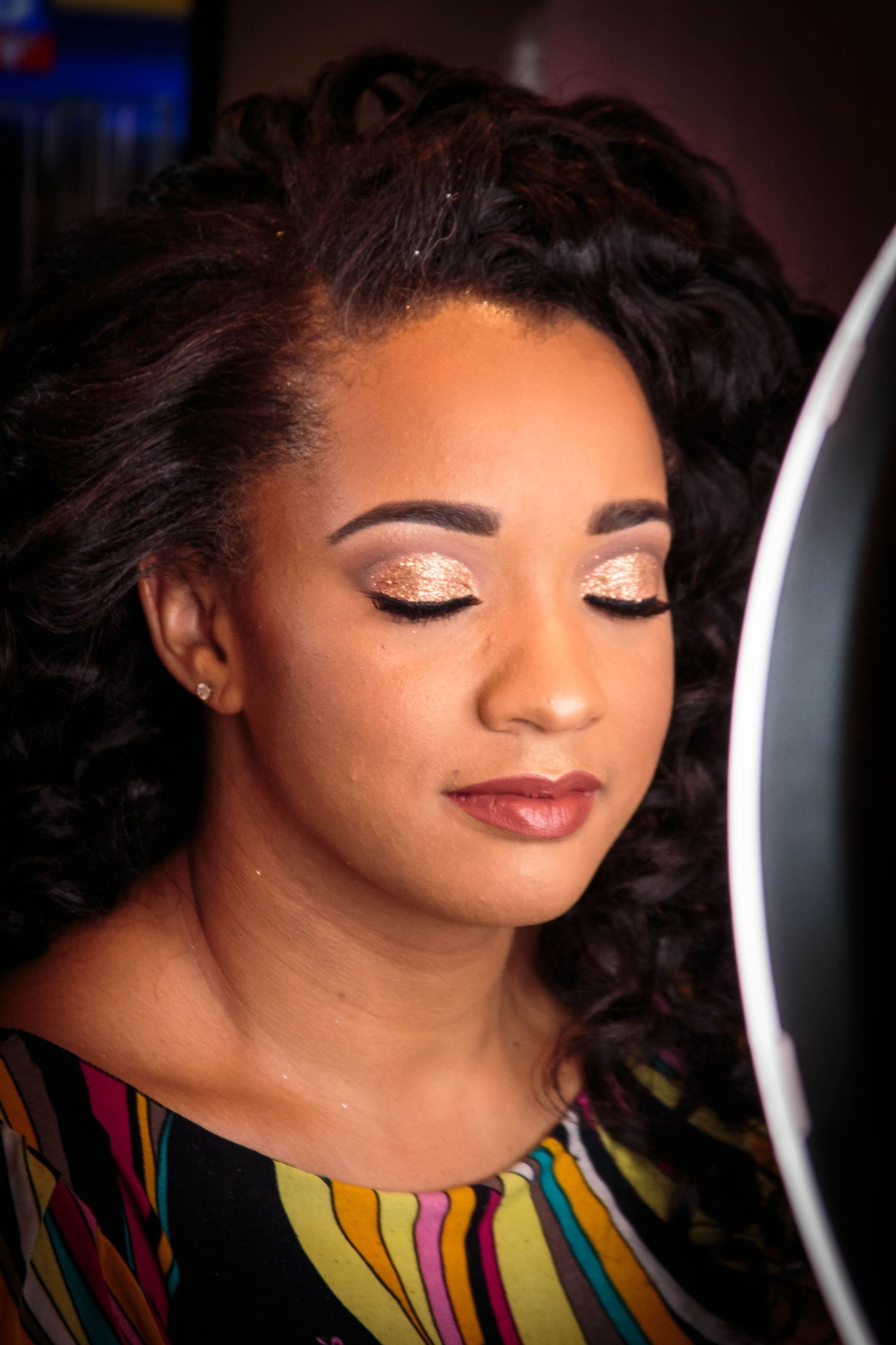 Beauty portrait showing shimmering eye makeup and styled curls against dark background.