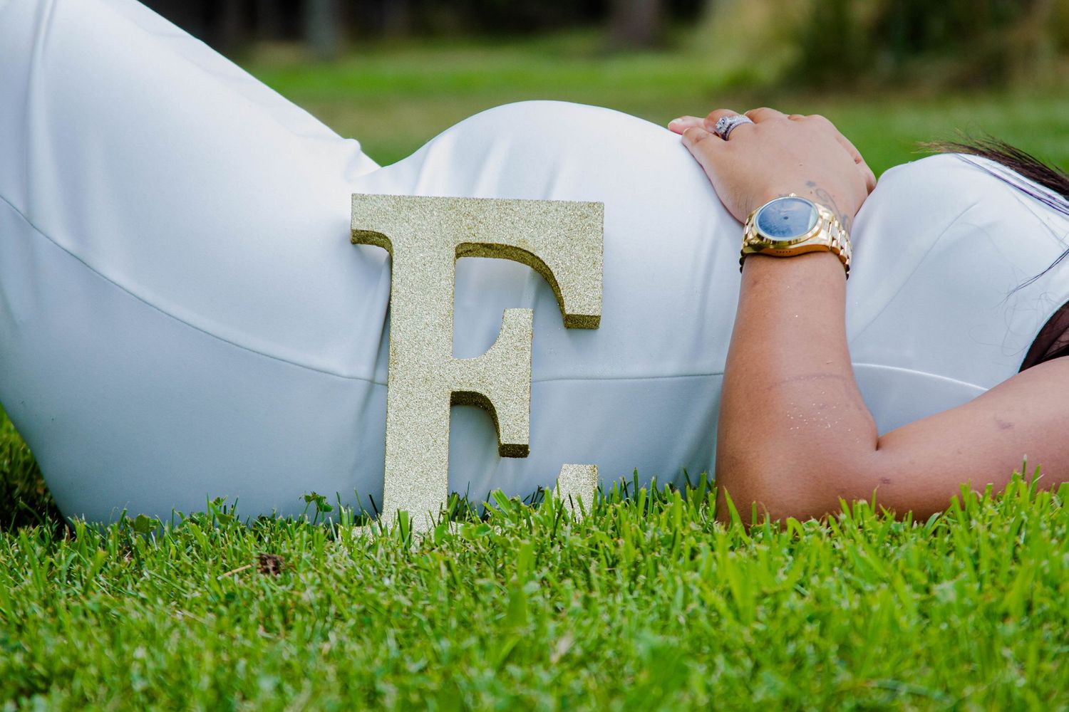 Creative maternity photo with letter F prop lying on green grass.