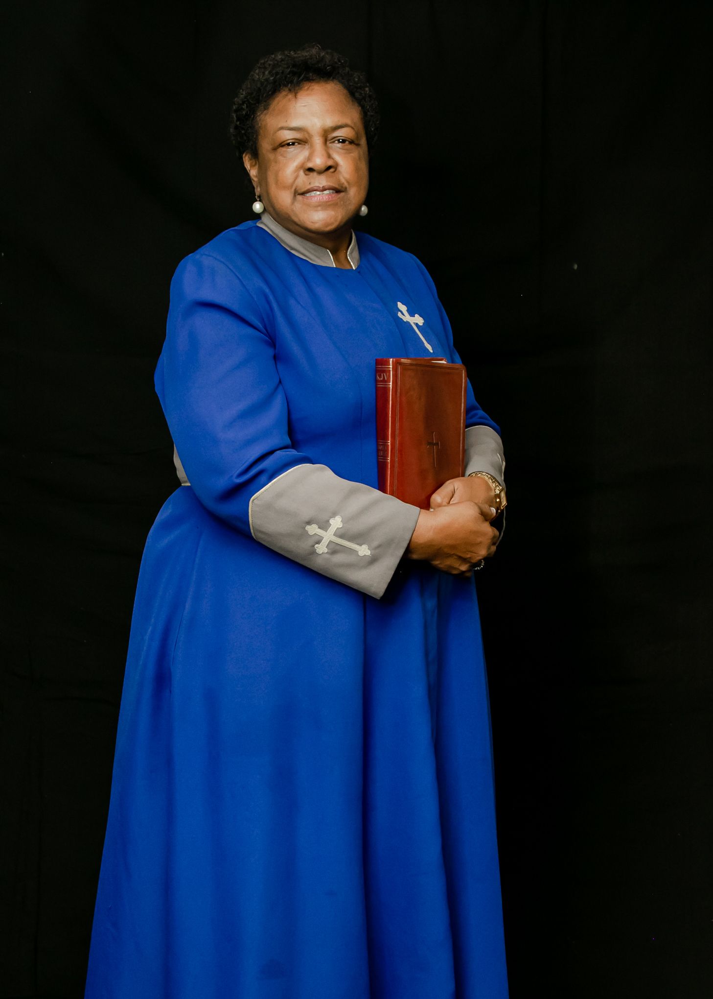 Professional portrait of person wearing a bright blue dress and holding a red book against dark background.