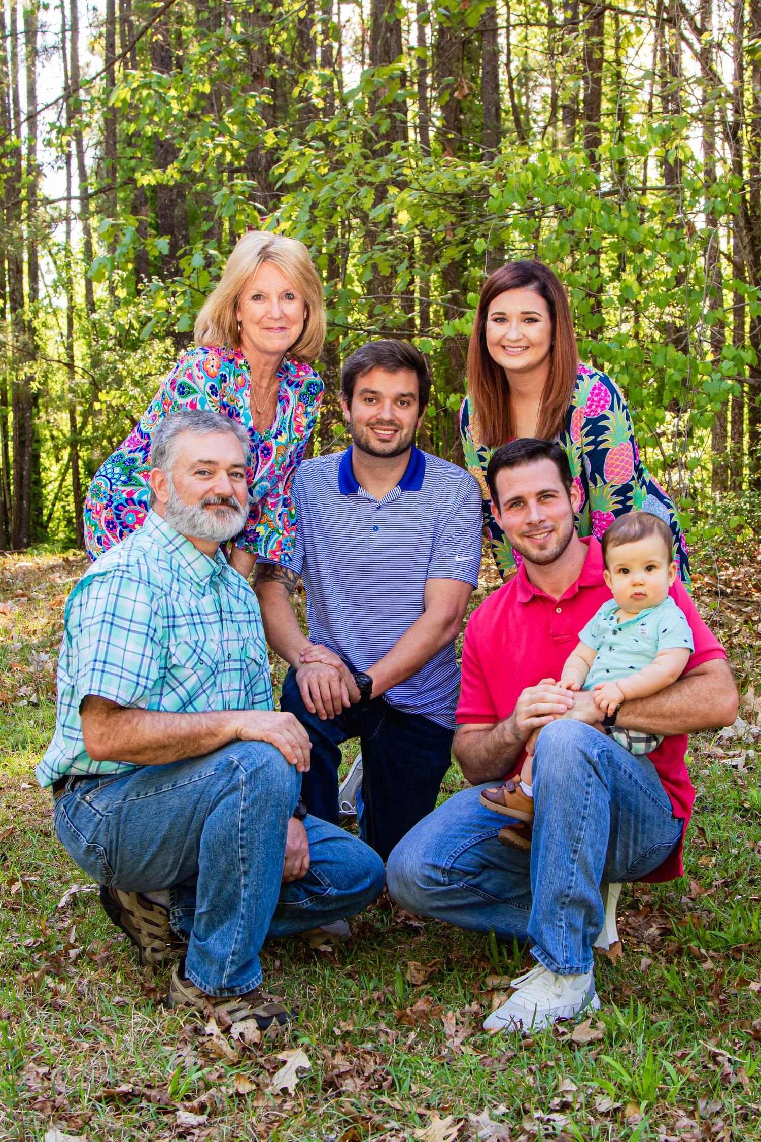 A multi-generational family photo taken in a forest setting with lush green trees in the background.