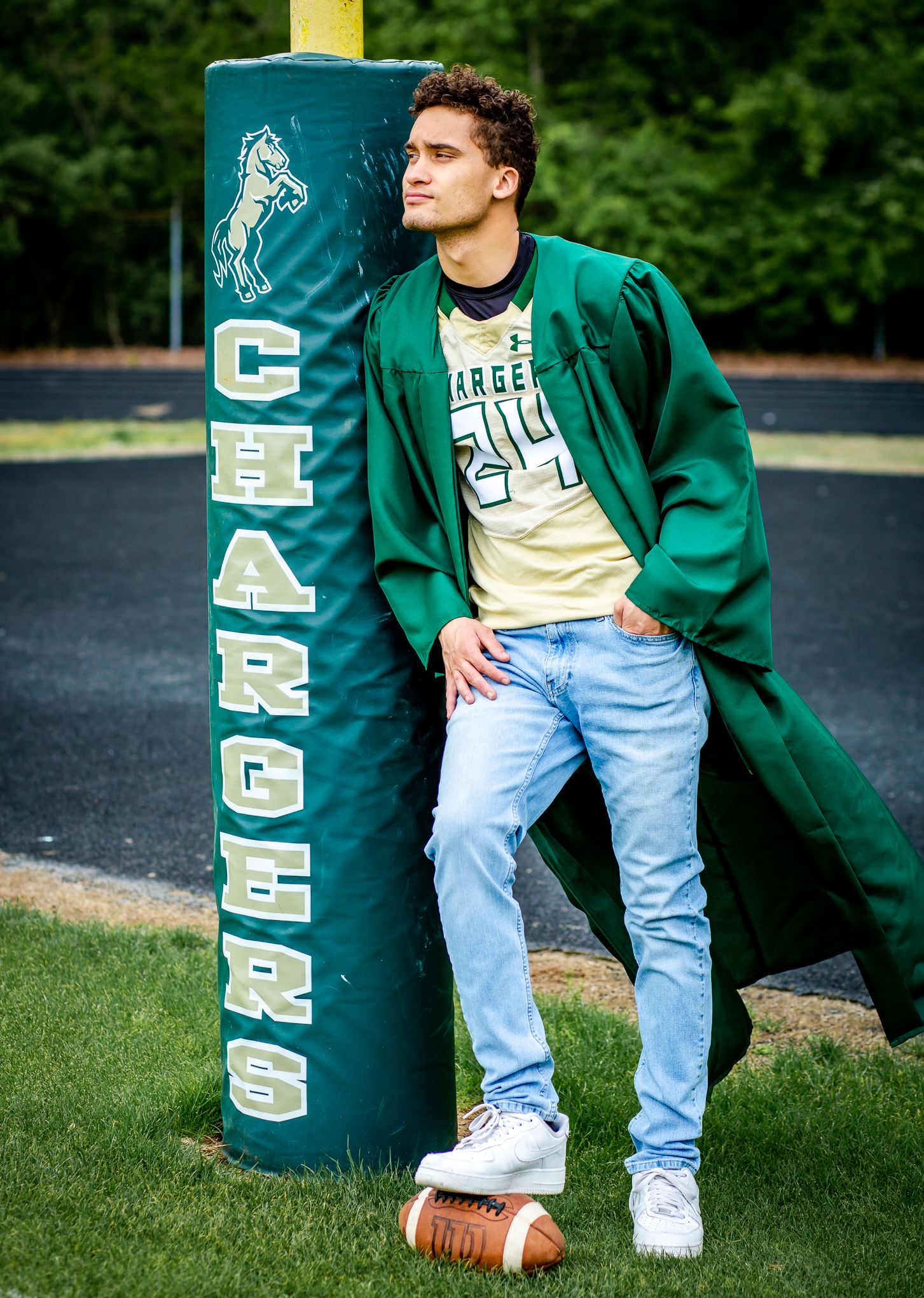 Athletic model in green varsity jacket leaning against Chargers football goal post.