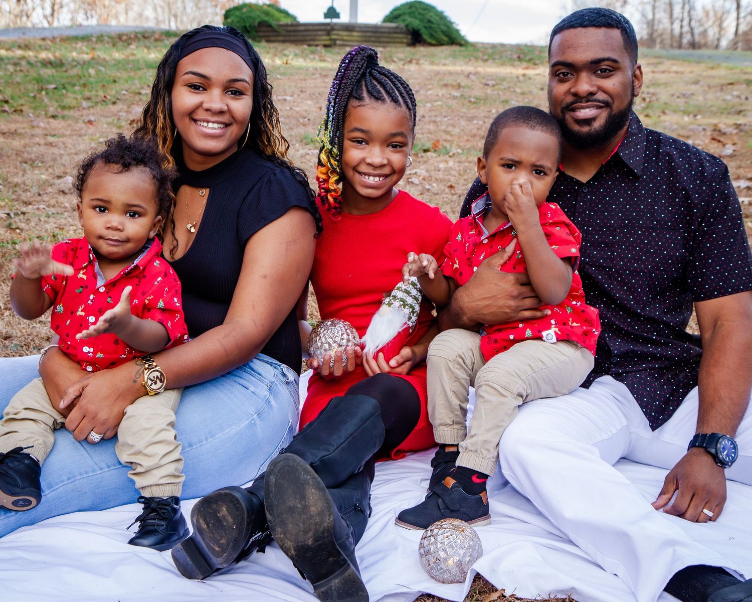A family of five sitting on a blanket outdoors wearing coordinated red and navy outfits.