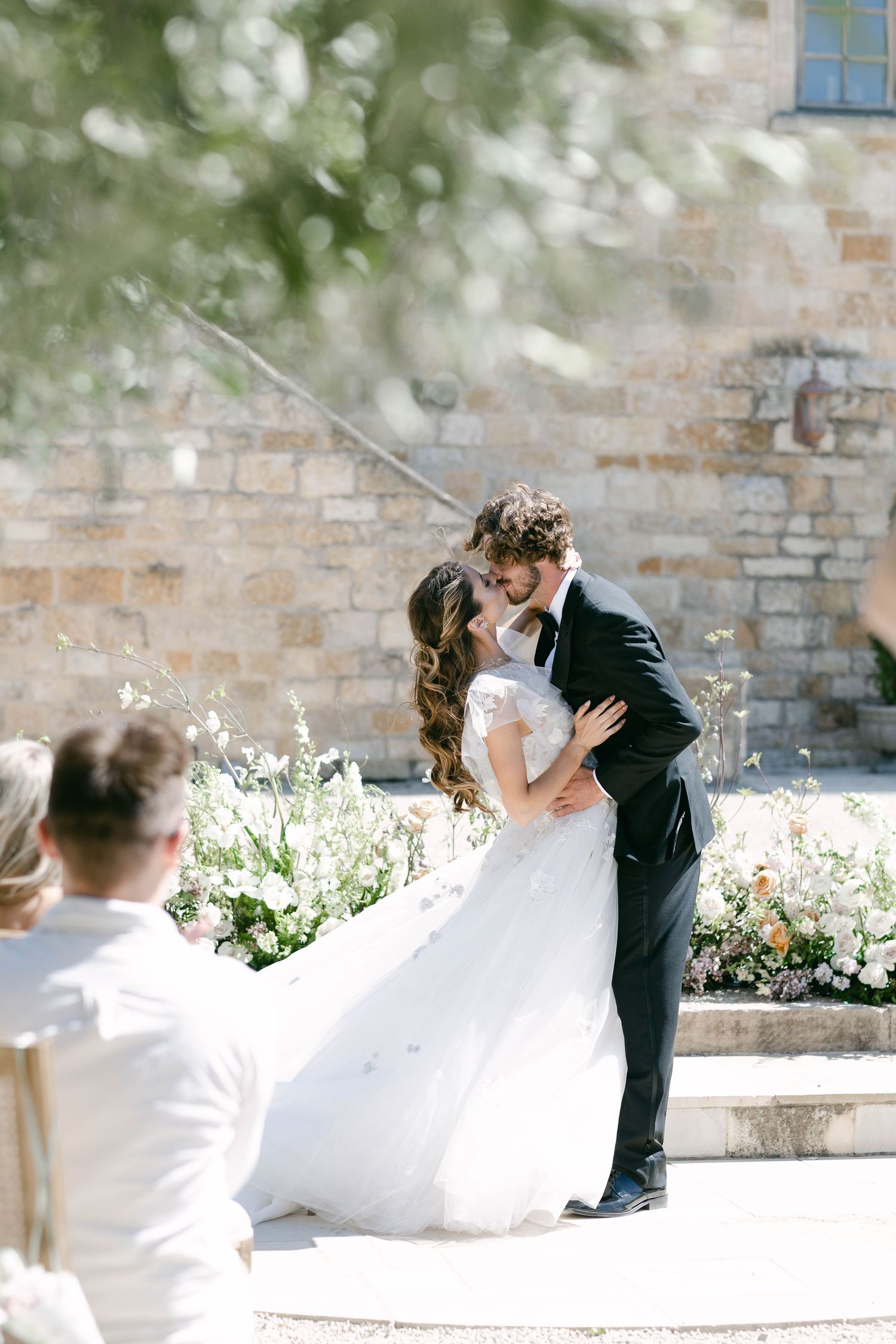 A joyful wedding celebration unfolds in front of a historic stone wall.