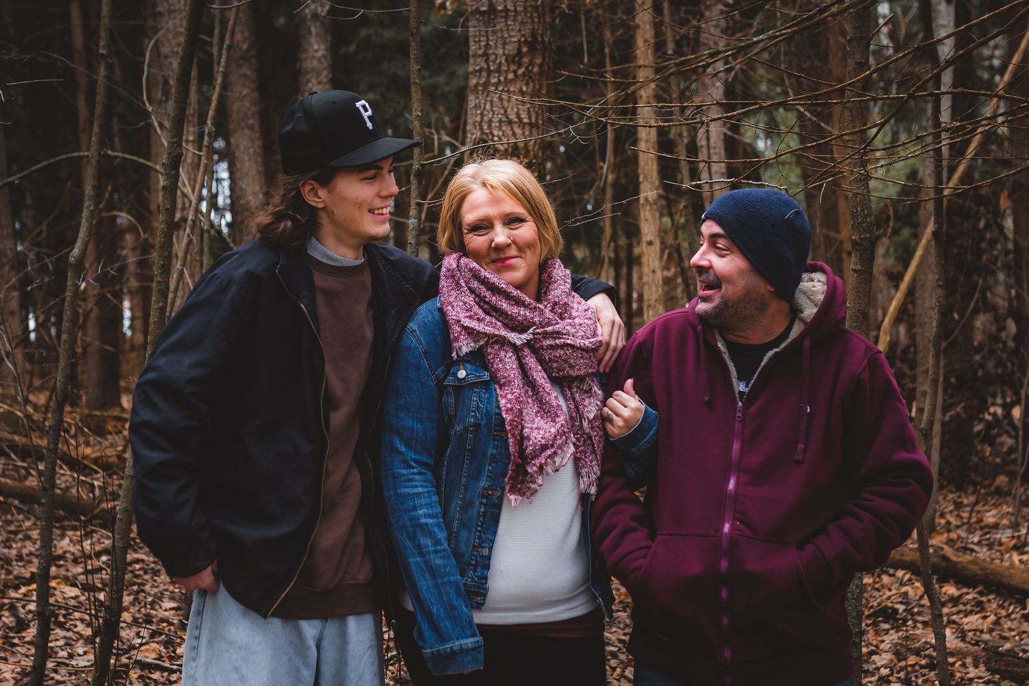 Woman smiling, linking arms with husband; teenage son on her other side with his arm around her in Roth Park, Woodstock