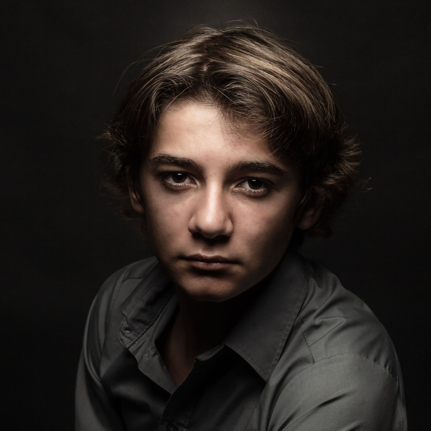 Moody low-key portrait against dark background featuring dramatic side lighting.