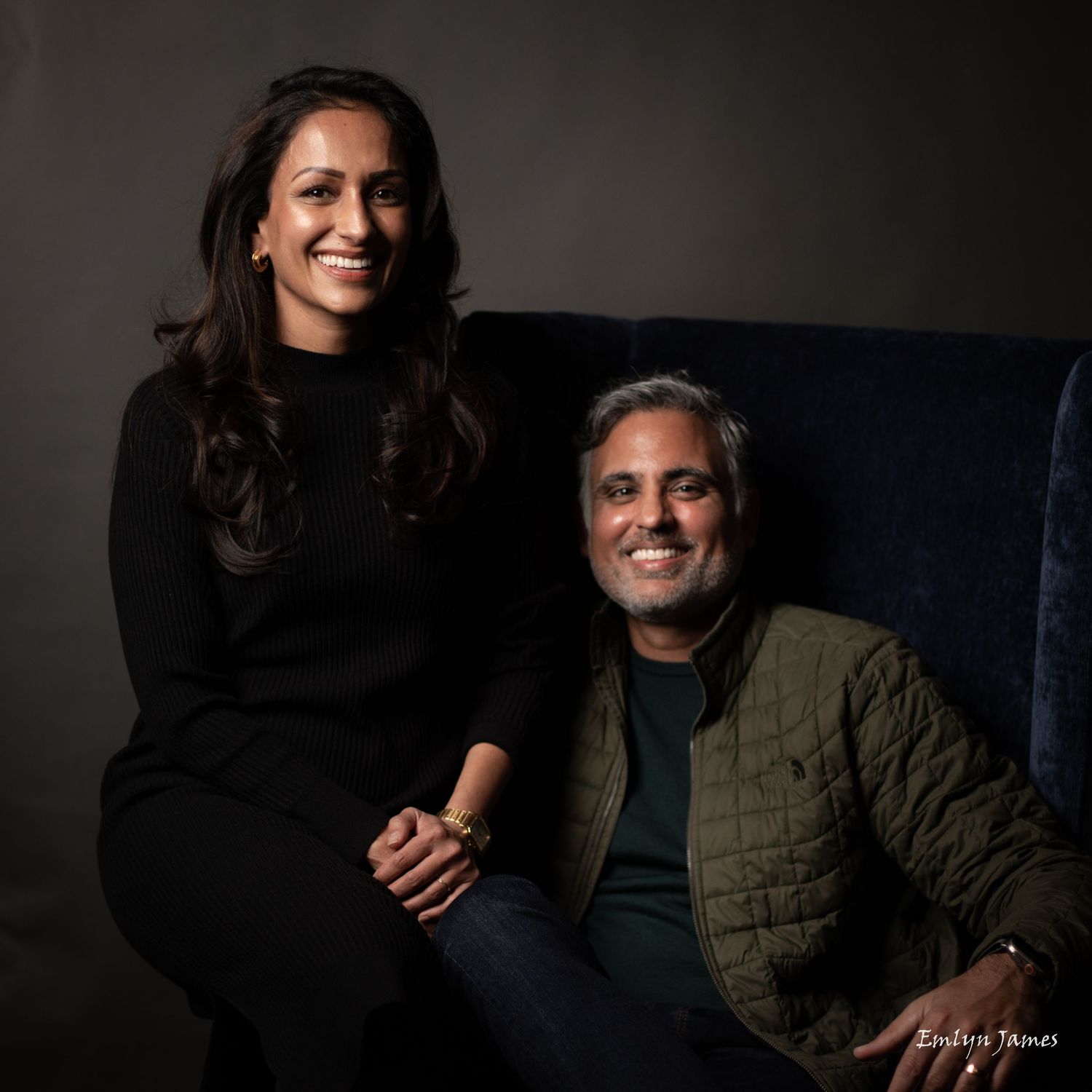 Warm studio portrait of a couple sitting together on blue furniture.