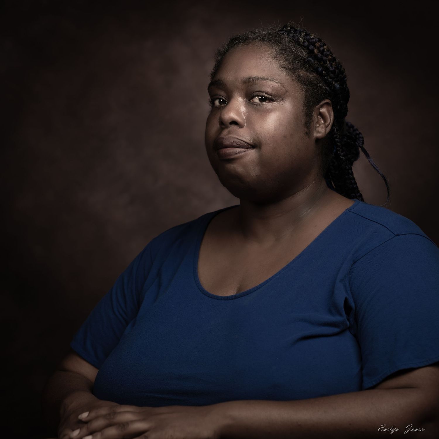 Dramatic studio portrait with dark background featuring a person wearing a navy blue top.