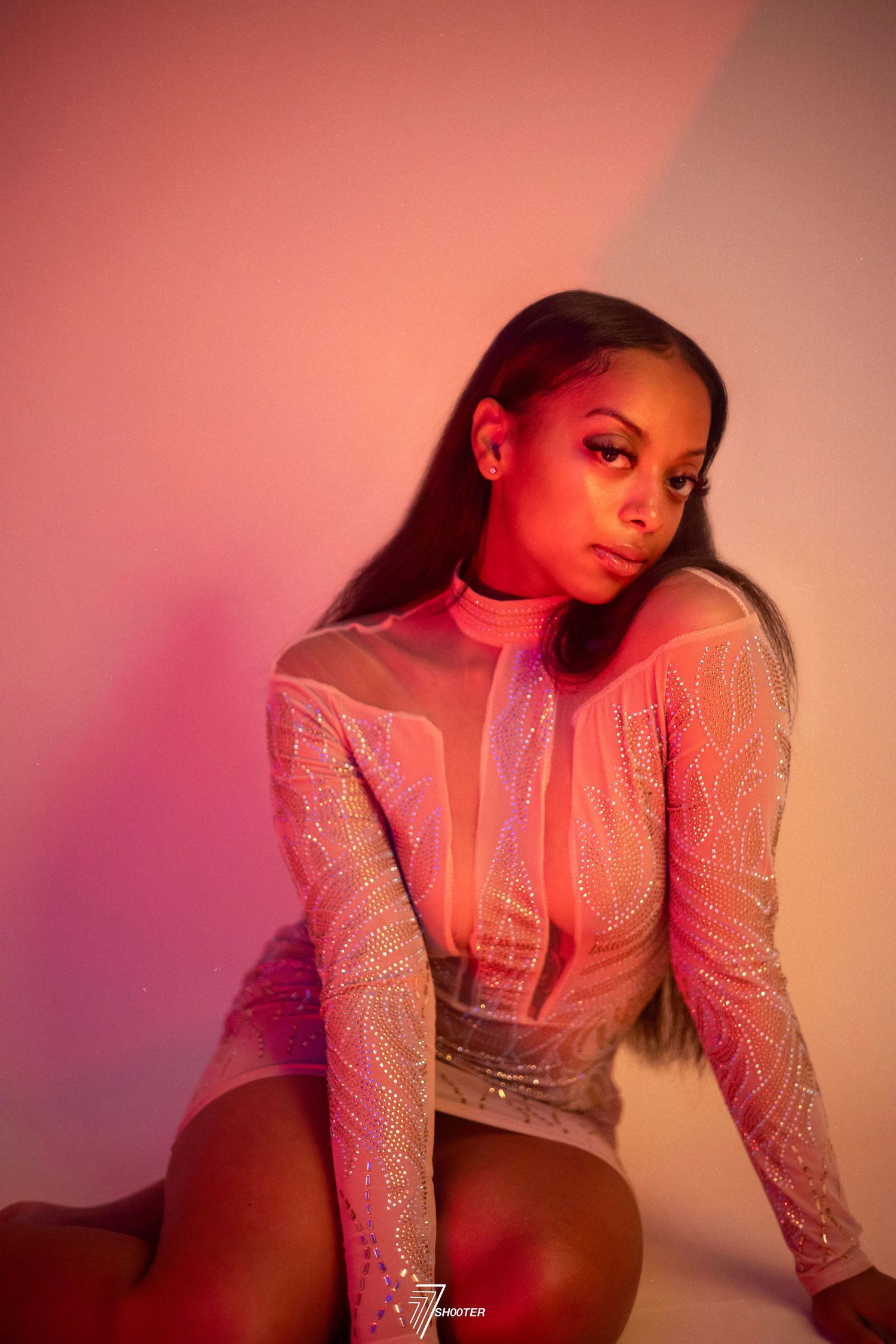 Fashion portrait with shimmering bodysuit in pink and red lighting against gradient background of coral tones.