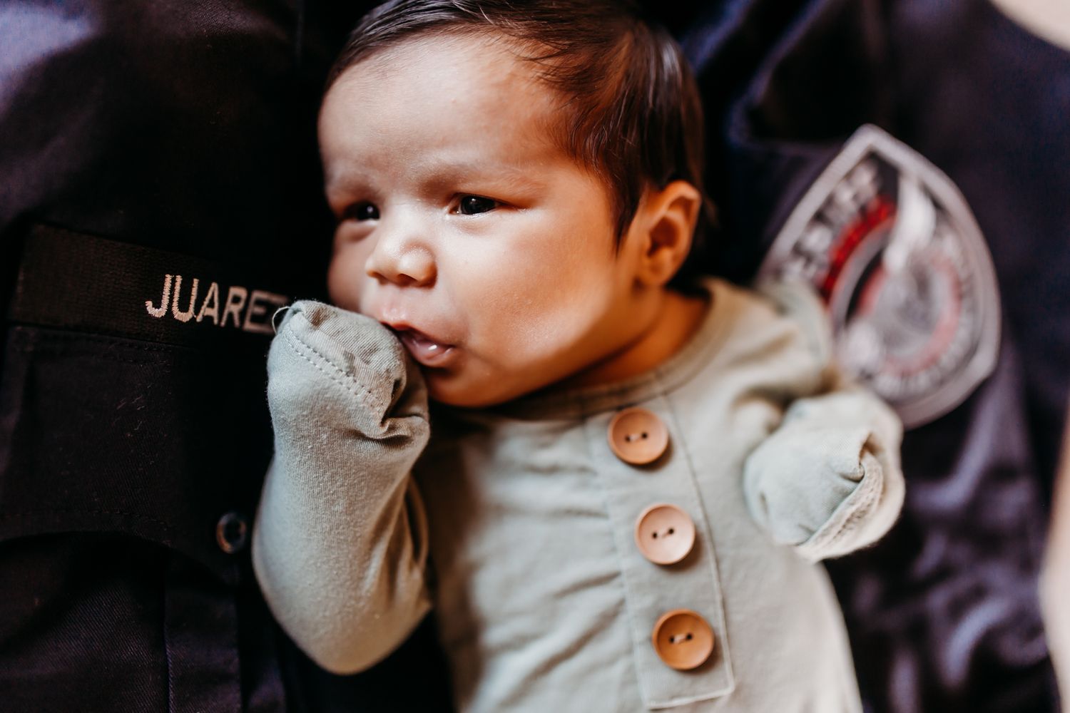A baby wearing a grey cardigan with wooden buttons chewing on their sleeve.