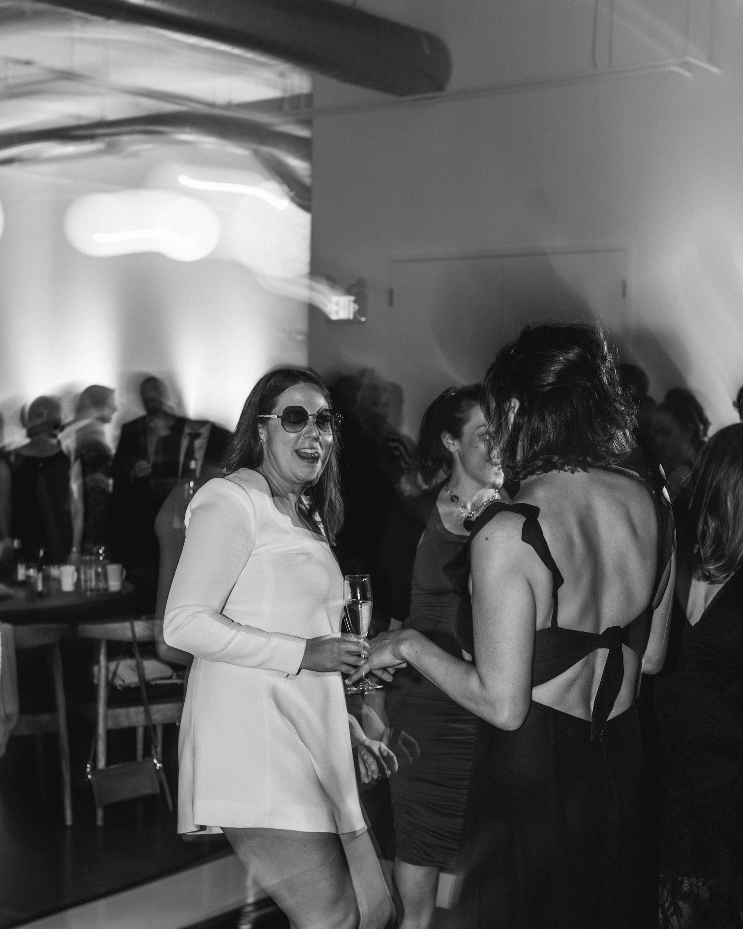 People dancing and socializing at a dimly lit party with white ceiling lights.