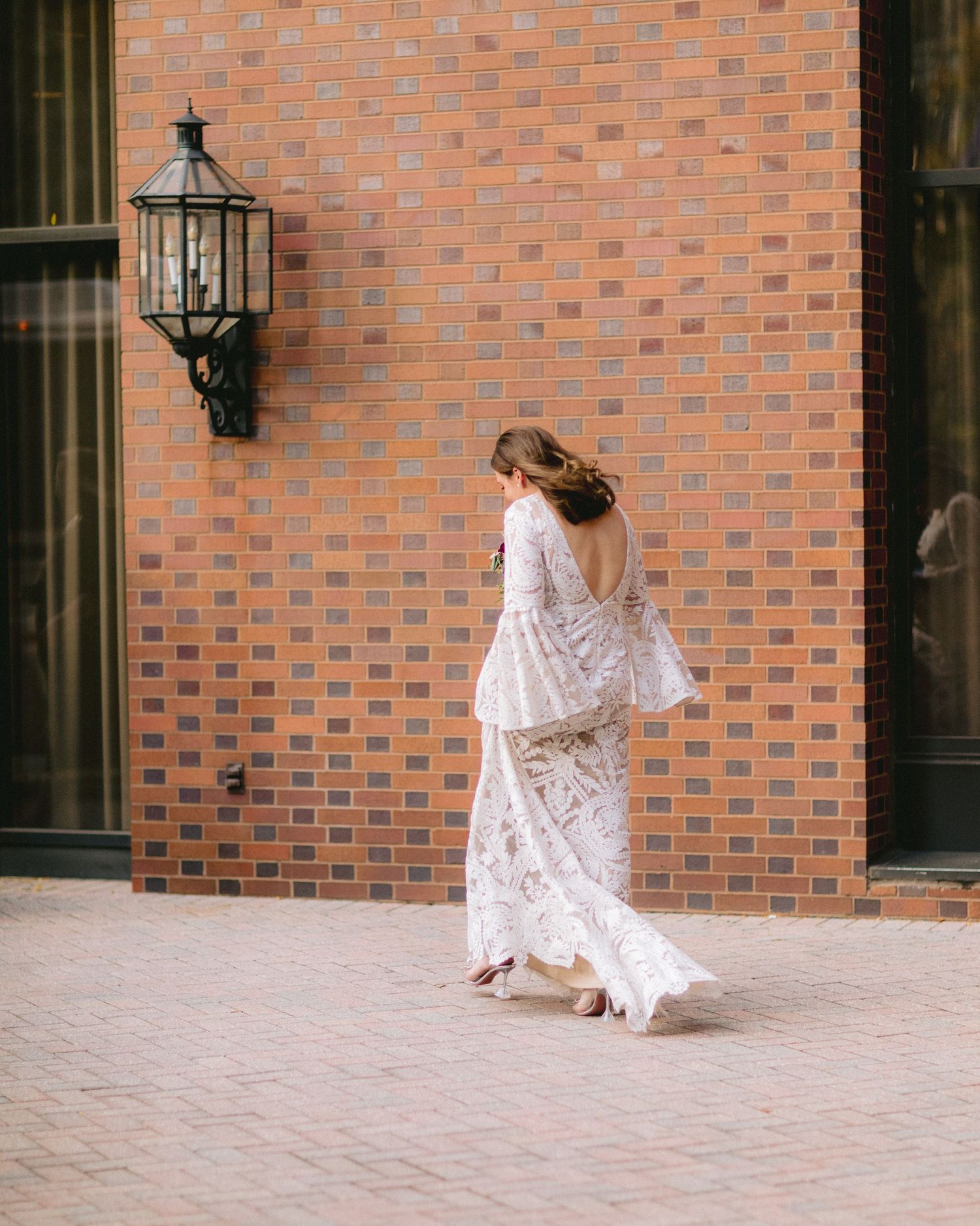 Elegant flowing white lace dress with flared sleeves photographed against a brick wall with vintage lantern.