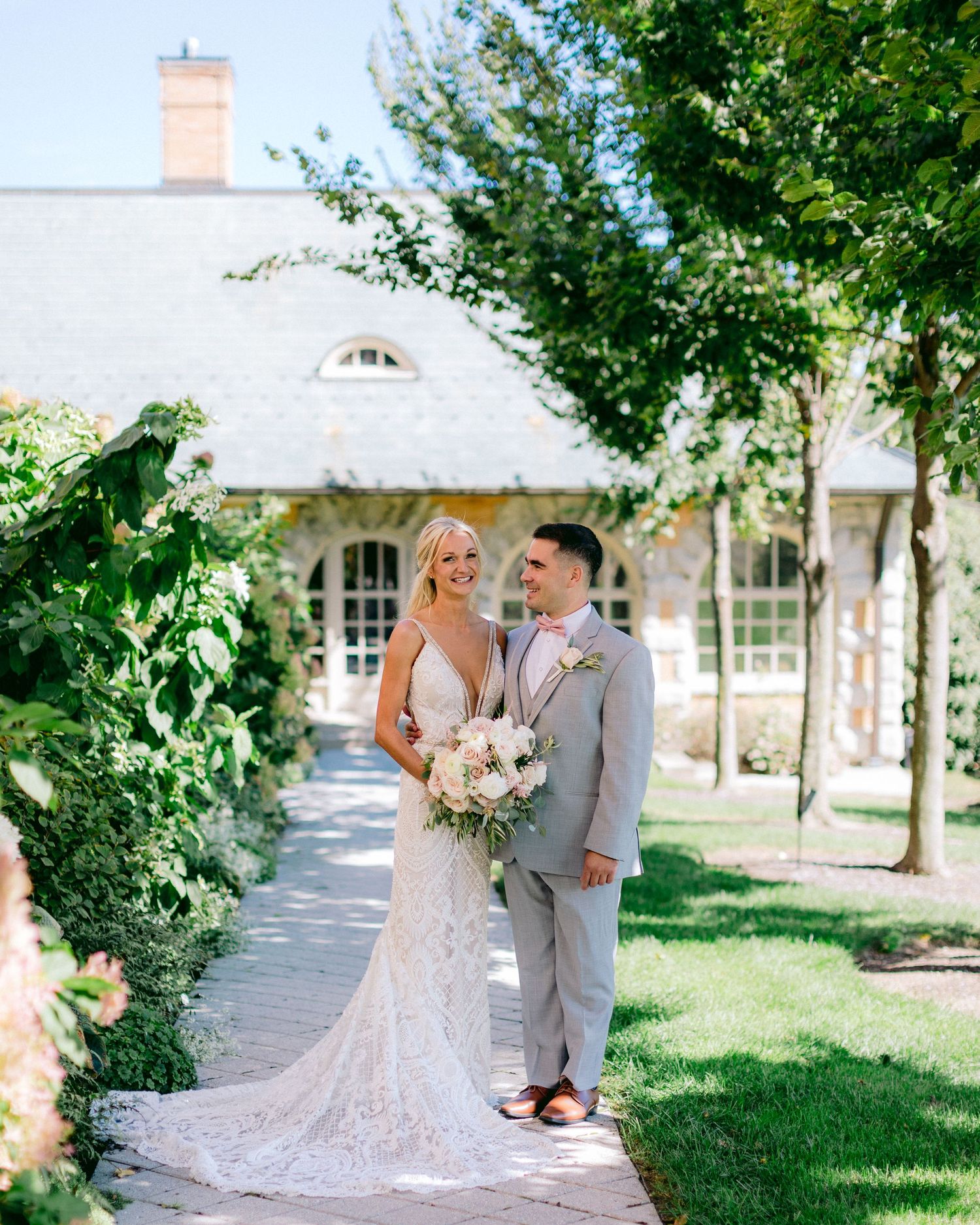 A couple poses in front of a charming cottage with climbing vines and a garden pathway.
