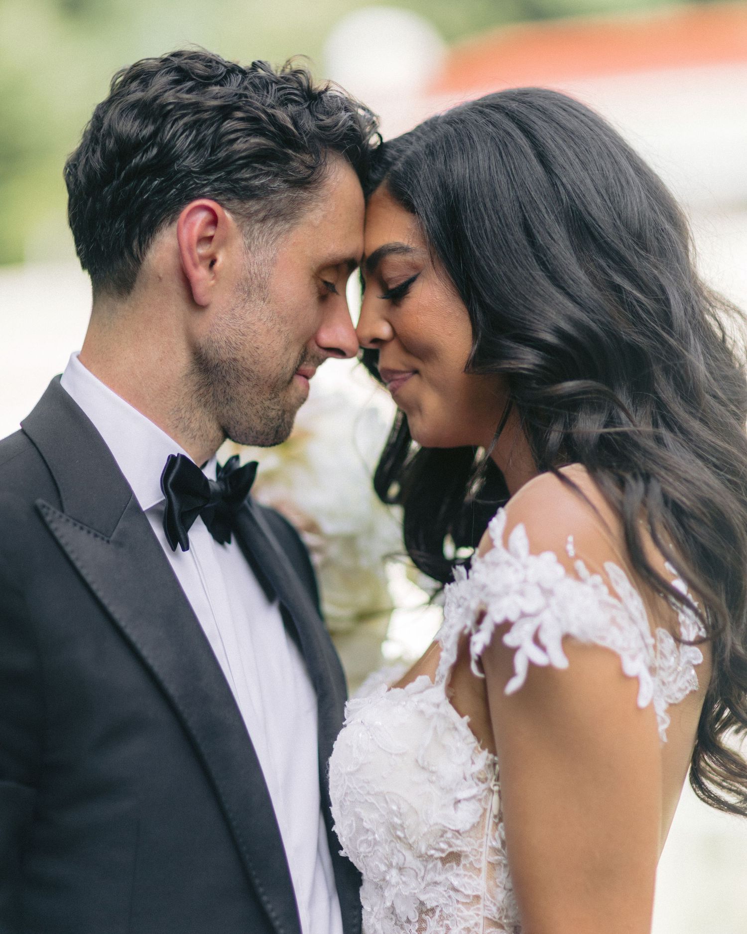 Romantic wedding couple shares intimate moment in elegant attire with lace dress and black tuxedo.