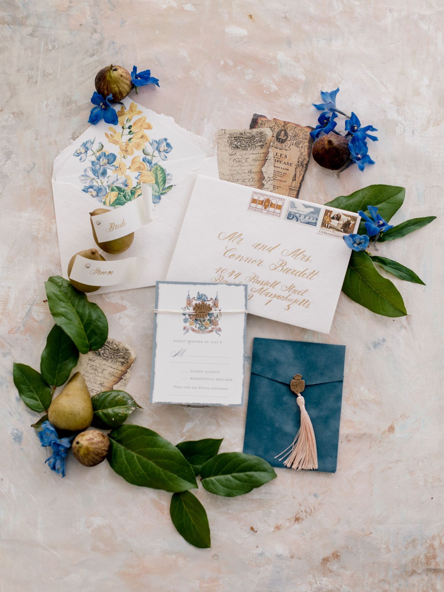 Elegant wedding invitation suite with blue flowers, pears, and greenery on a light textured background.