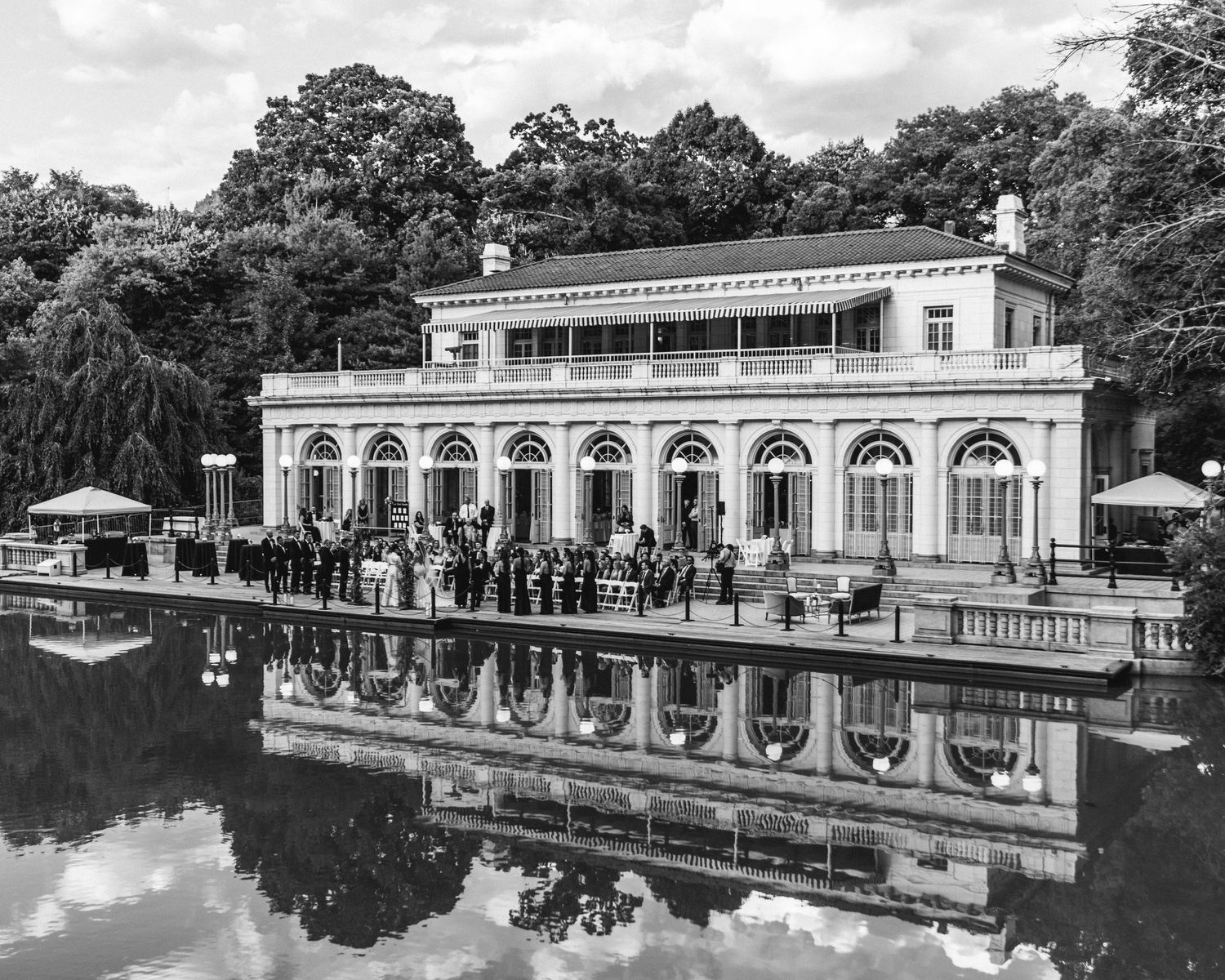 Historic boathouse with white columns reflected in a lake at a wedding venue.