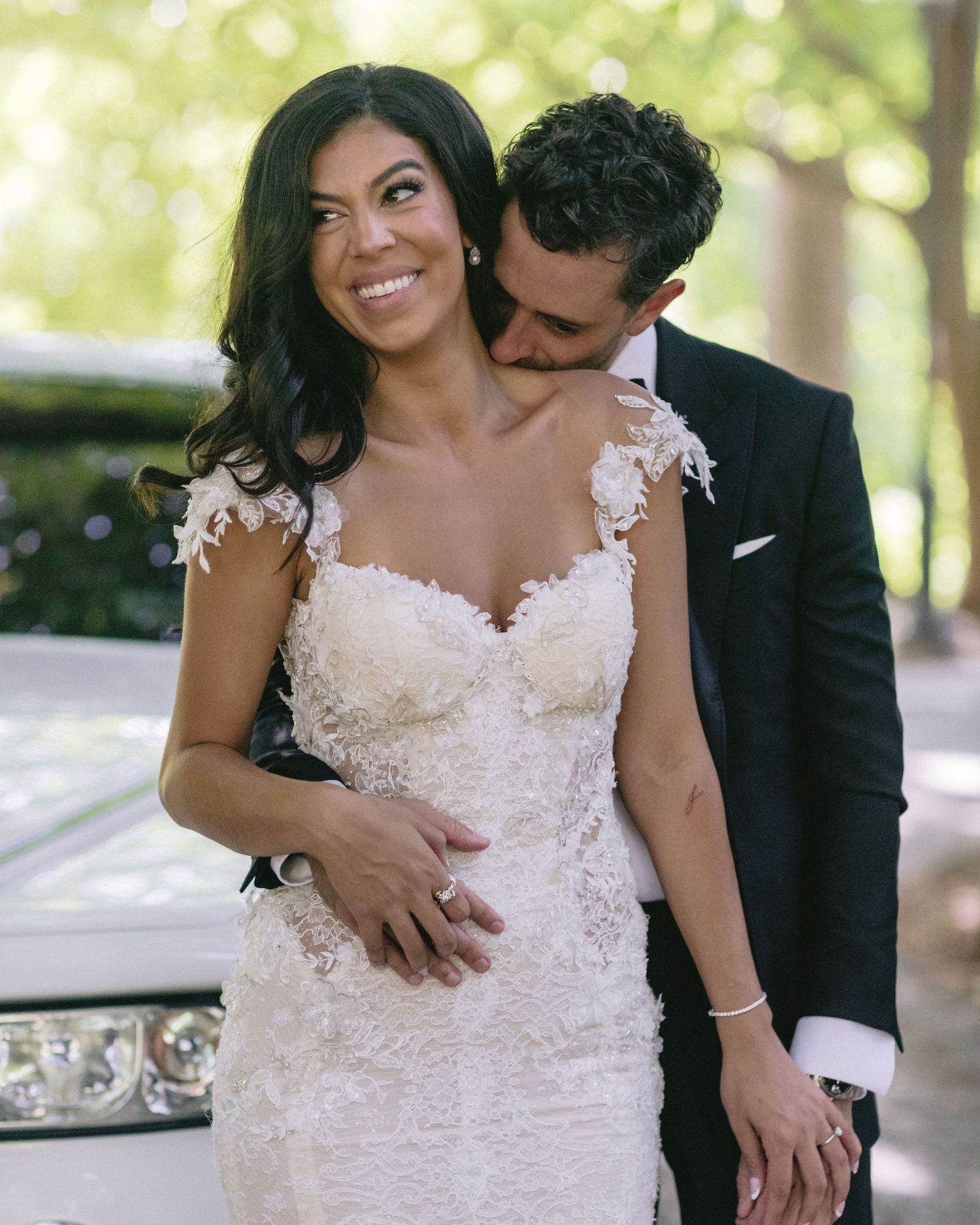 Joyful wedding portrait with bride in lace dress embraced from behind.